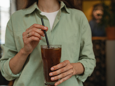Close-up of woman in green linen shirt drinking summer refreshing beverage. A woman mixing espresso tonic with a straw.