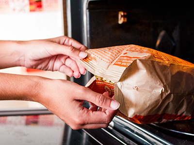 Woman hands taking a cooked popcorn bag from the microwave