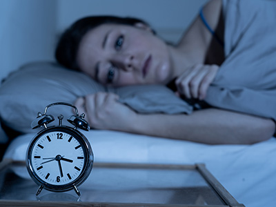 Sleepless and desperate beautiful caucasian woman awake at night not able to sleep, feeling frustrated and worried looking at clock suffering from insomnia in sleep disorder concept.