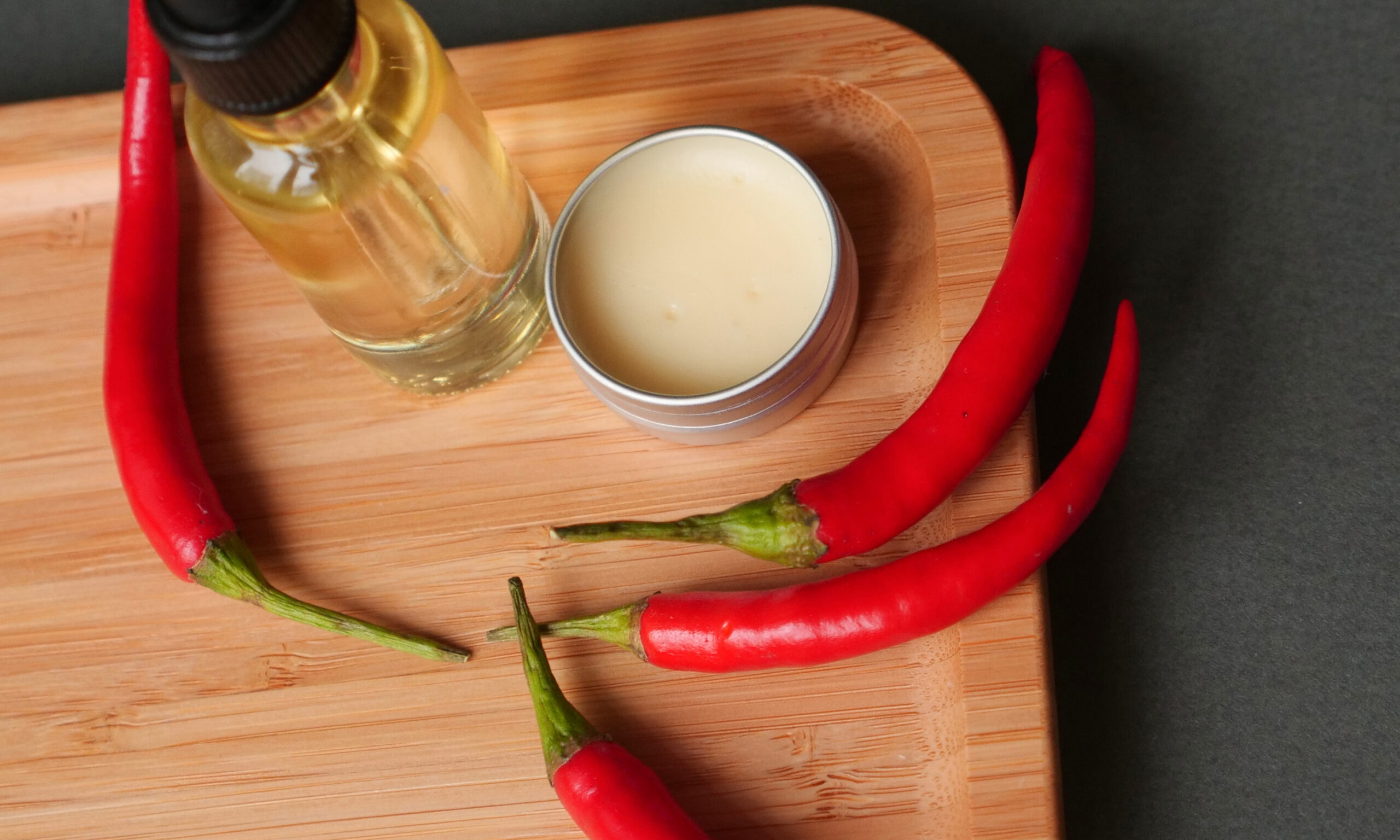 oil beard and mustache for grooming, wax jar with red chilli pepper on wood tray, grey background. Concept men cosmetic, barber shop tool, close up