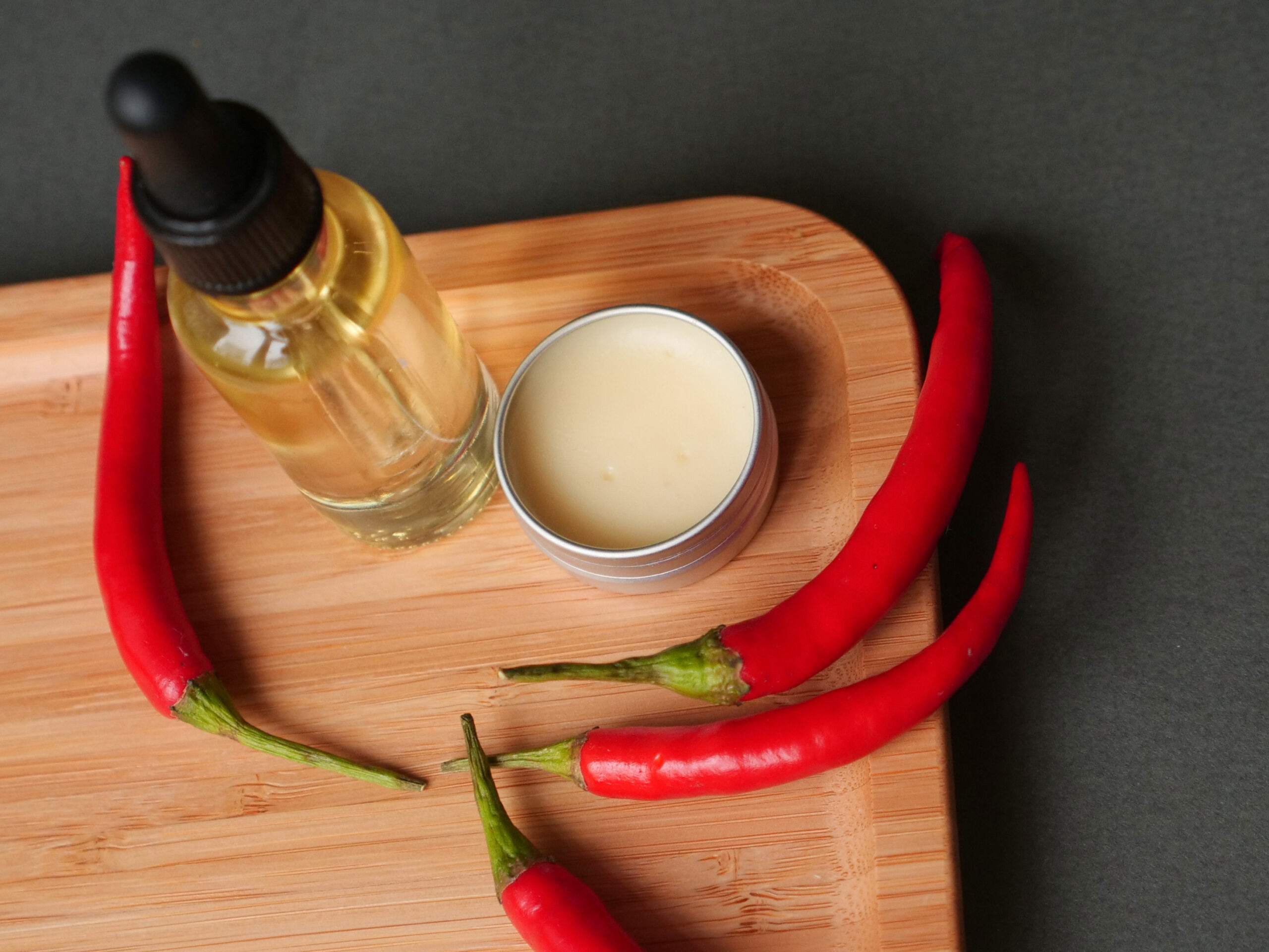 oil beard and mustache for grooming, wax jar with red chilli pepper on wood tray, grey background. Concept men cosmetic, barber shop tool, close up