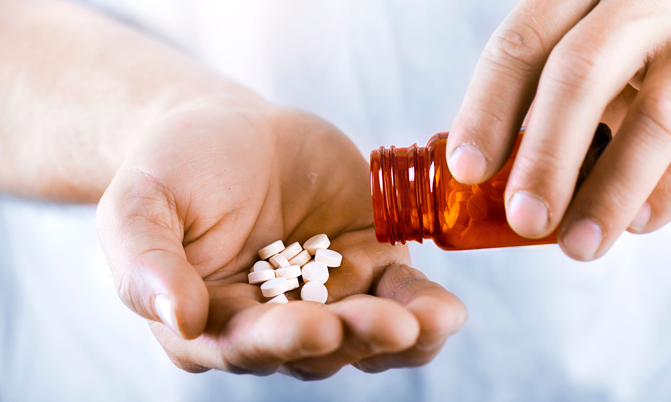 Hand holding on open palm with pill tablets medicine for healing. Man takes medicines with glass of water.
