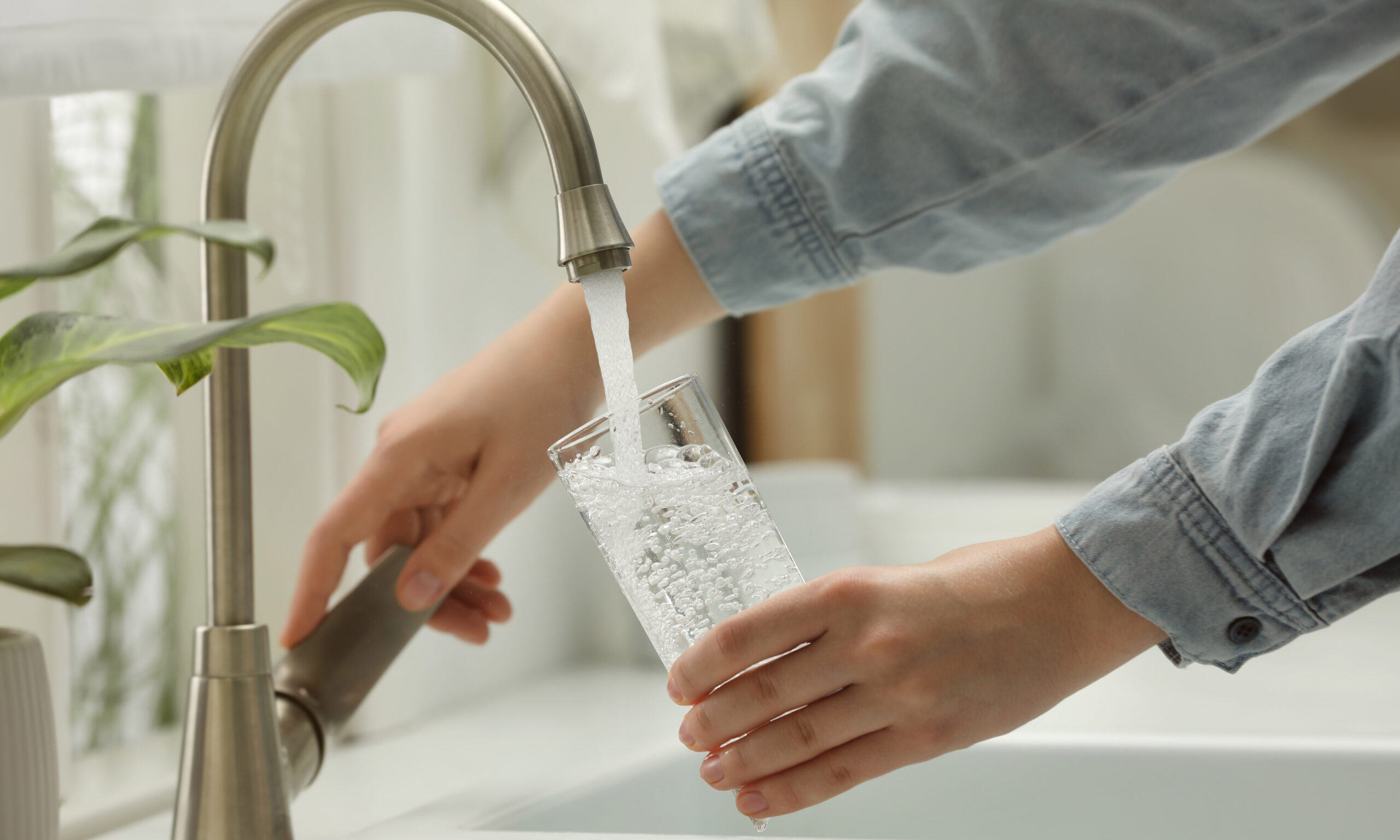 Woman filling glass with water from tap at home, closeup