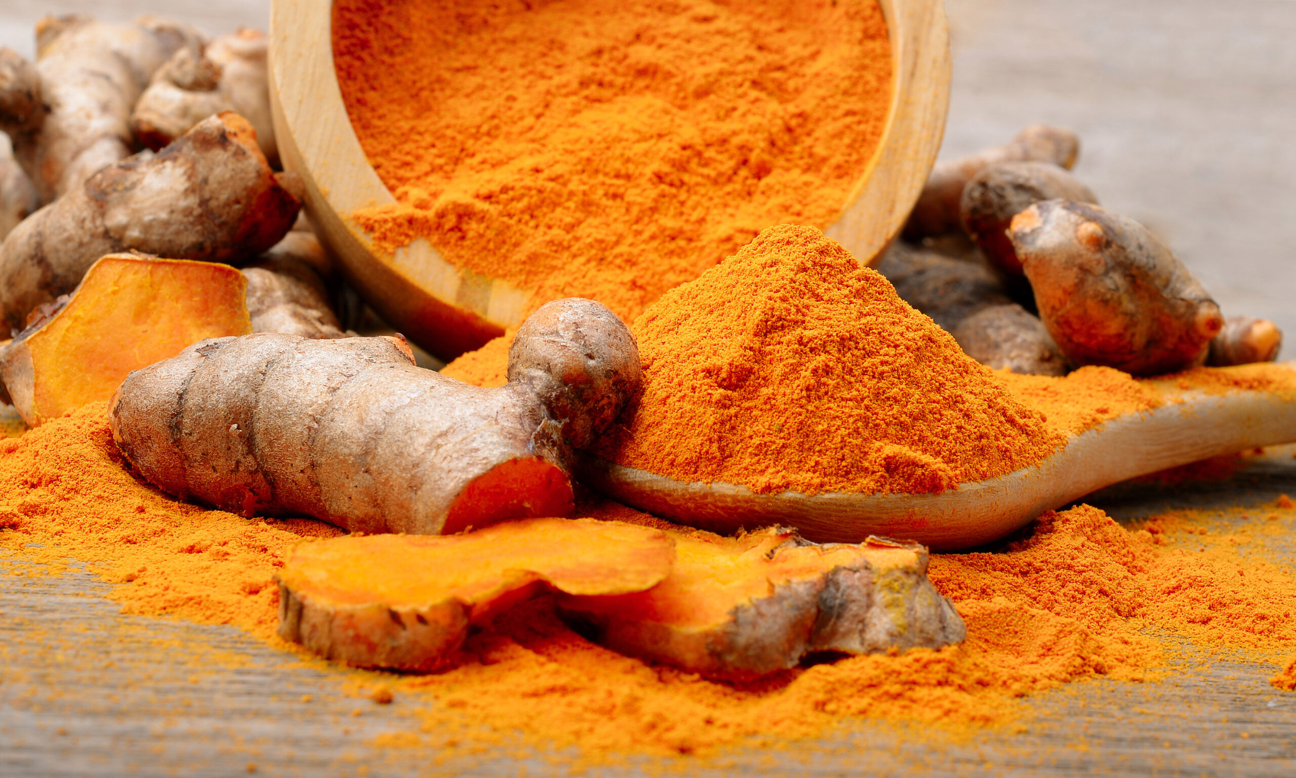 Turmeric powder and fresh turmeric on wooden background.