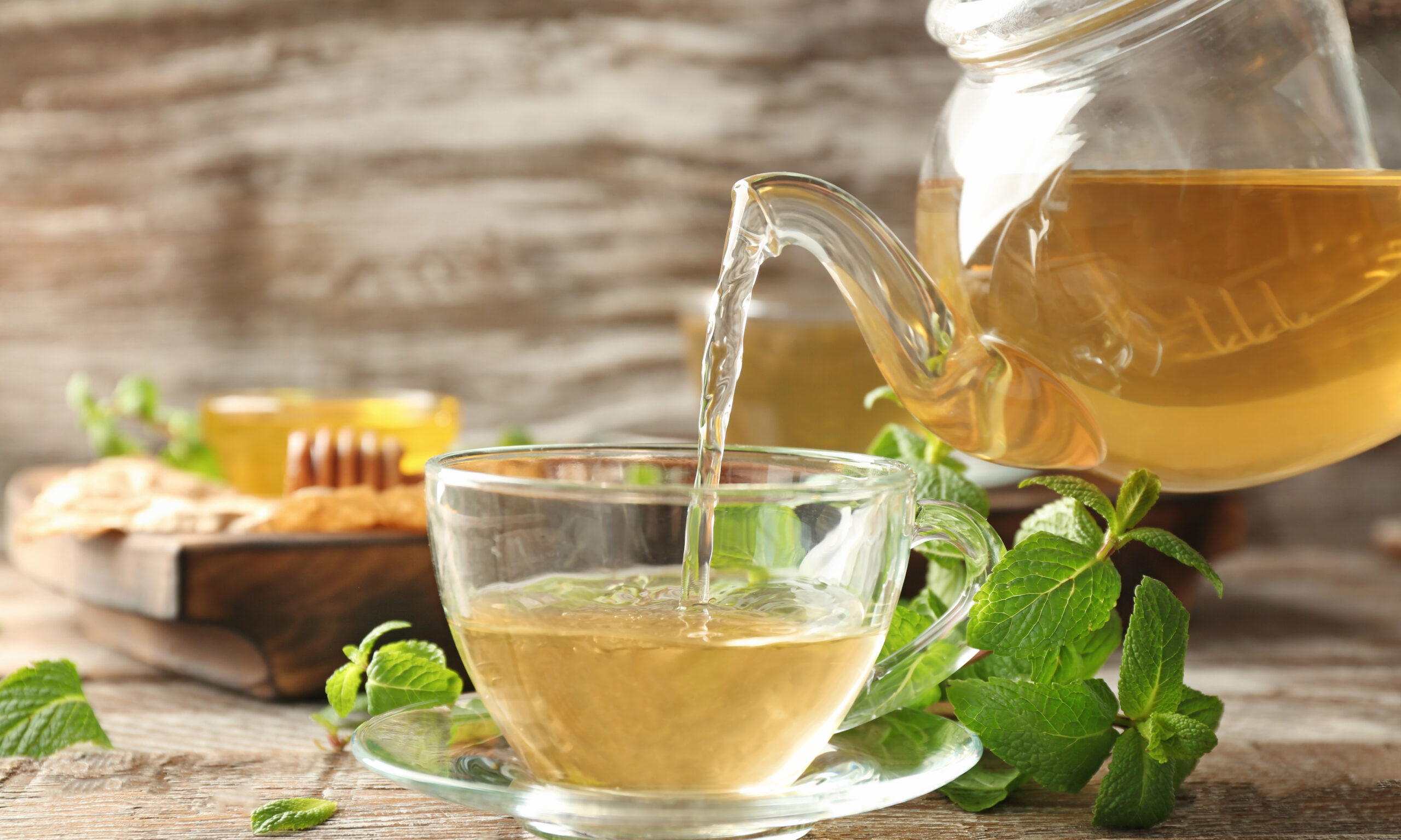 Pouring aromatic lemon balm tea into cup on wooden table