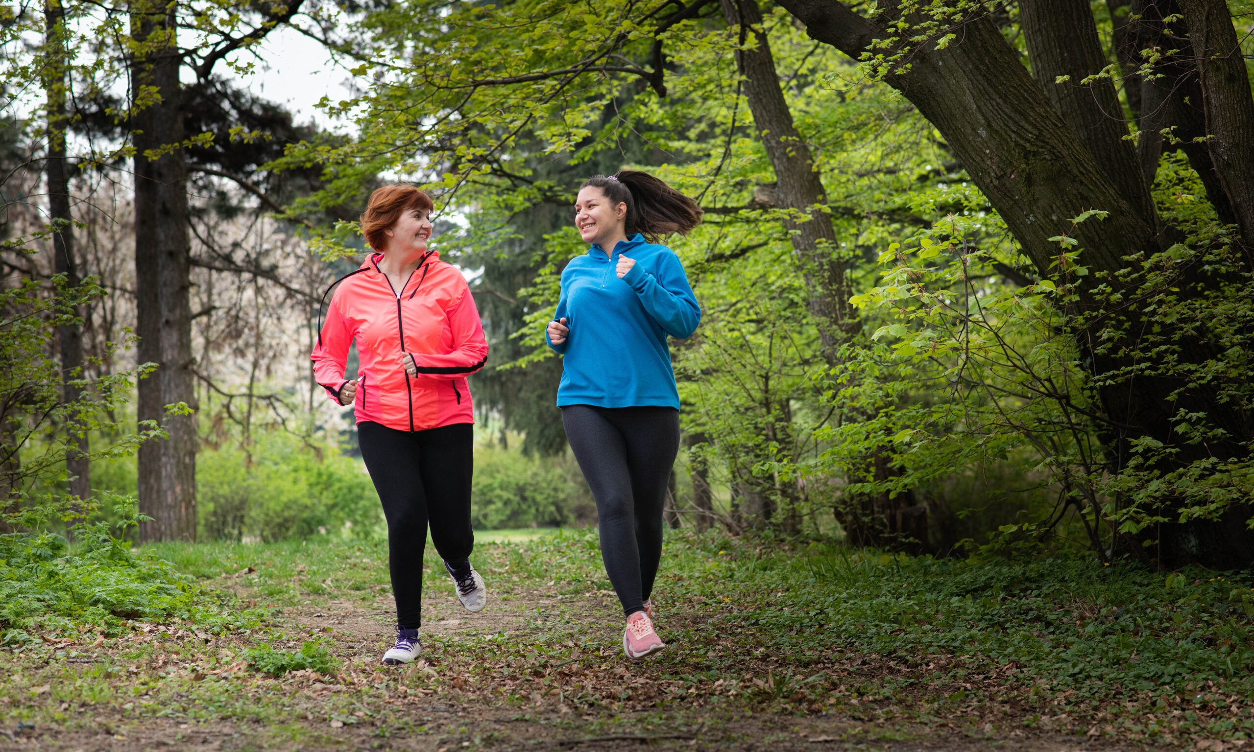 Mother and daughter wearing sportswear and running in forest at mountain