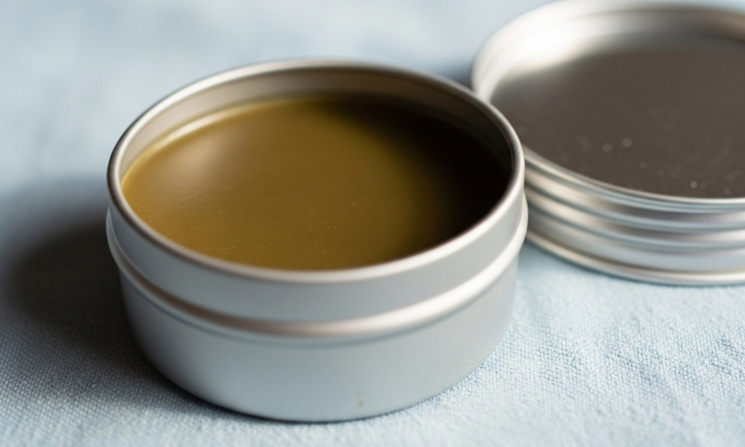 Homemade Herbal Balm in Metal Tin on Light Blue Fabric