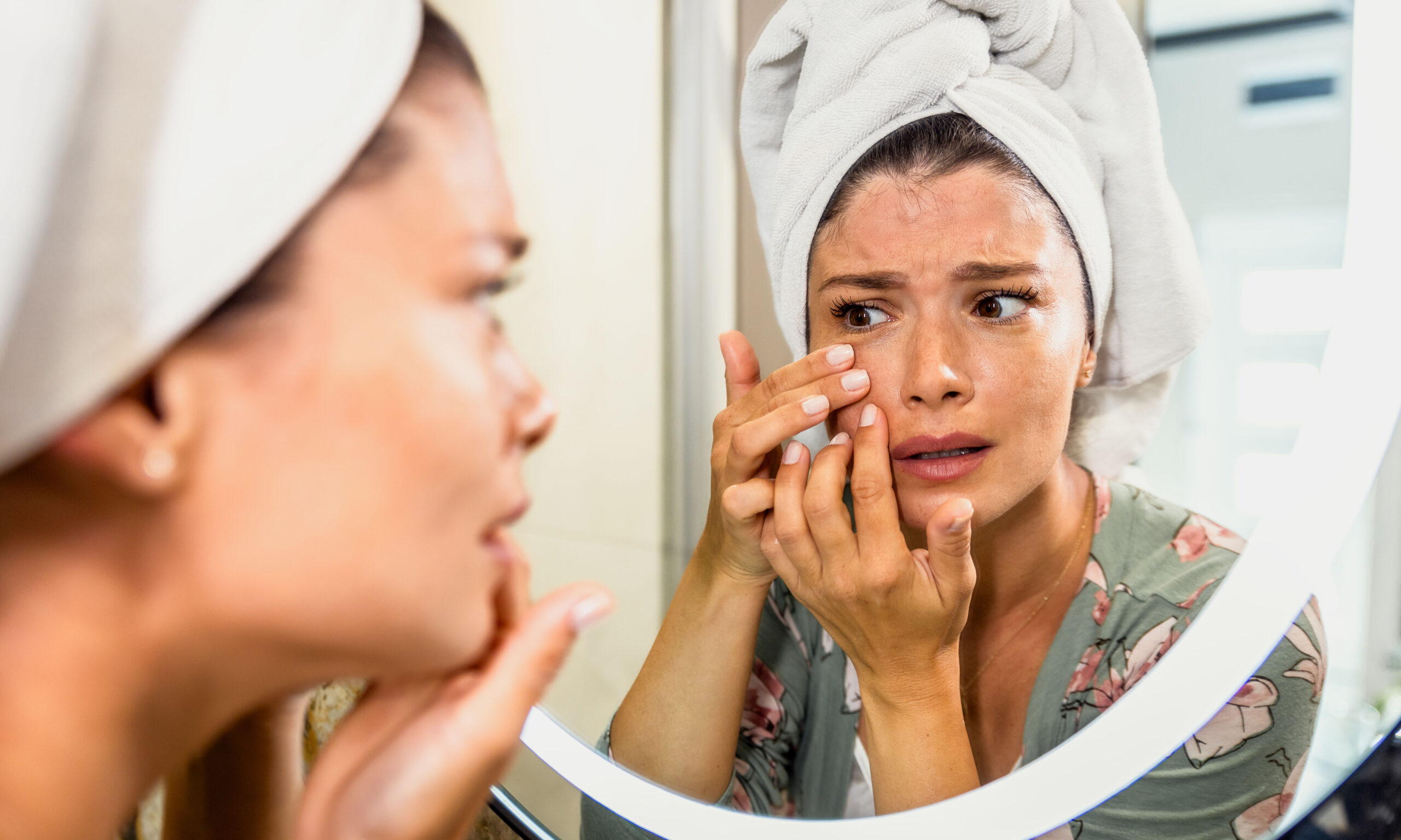 Worried woman looking in bathroom mirror worried about wrinkles and aging.