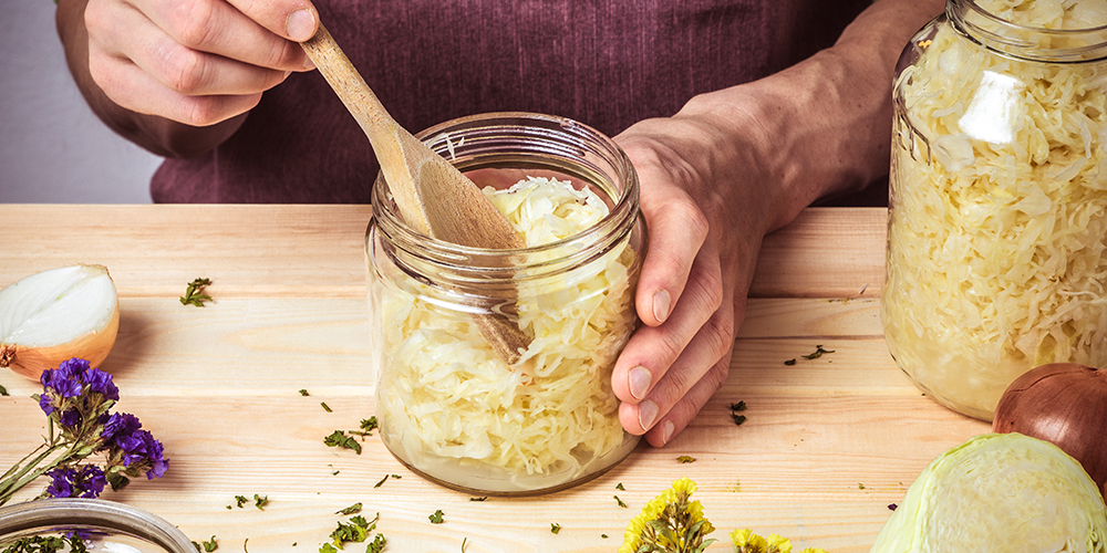 The cook puts sauerkraut in glass jars. On the table are spices,