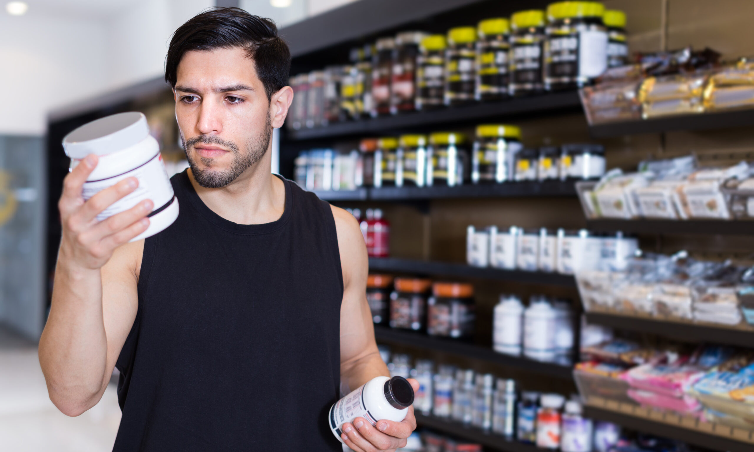 Serious young muscular sportman looking sport dietary supplements in store