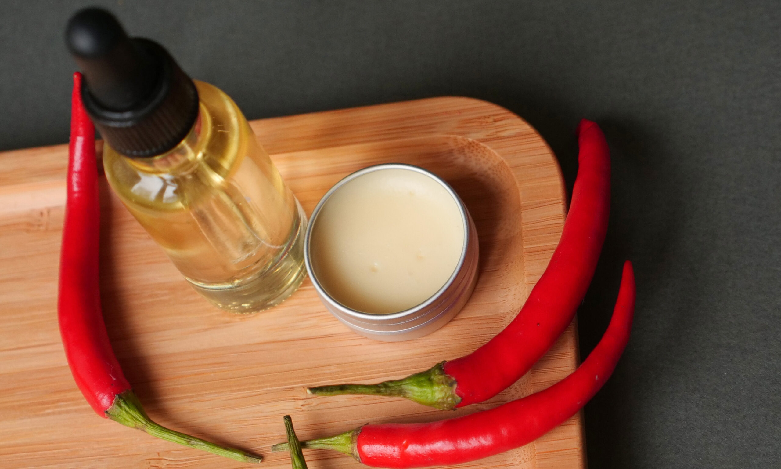 oil beard and mustache for grooming, wax jar with red chilli pepper on wood tray, grey background. Concept men cosmetic, barber shop tool, close up