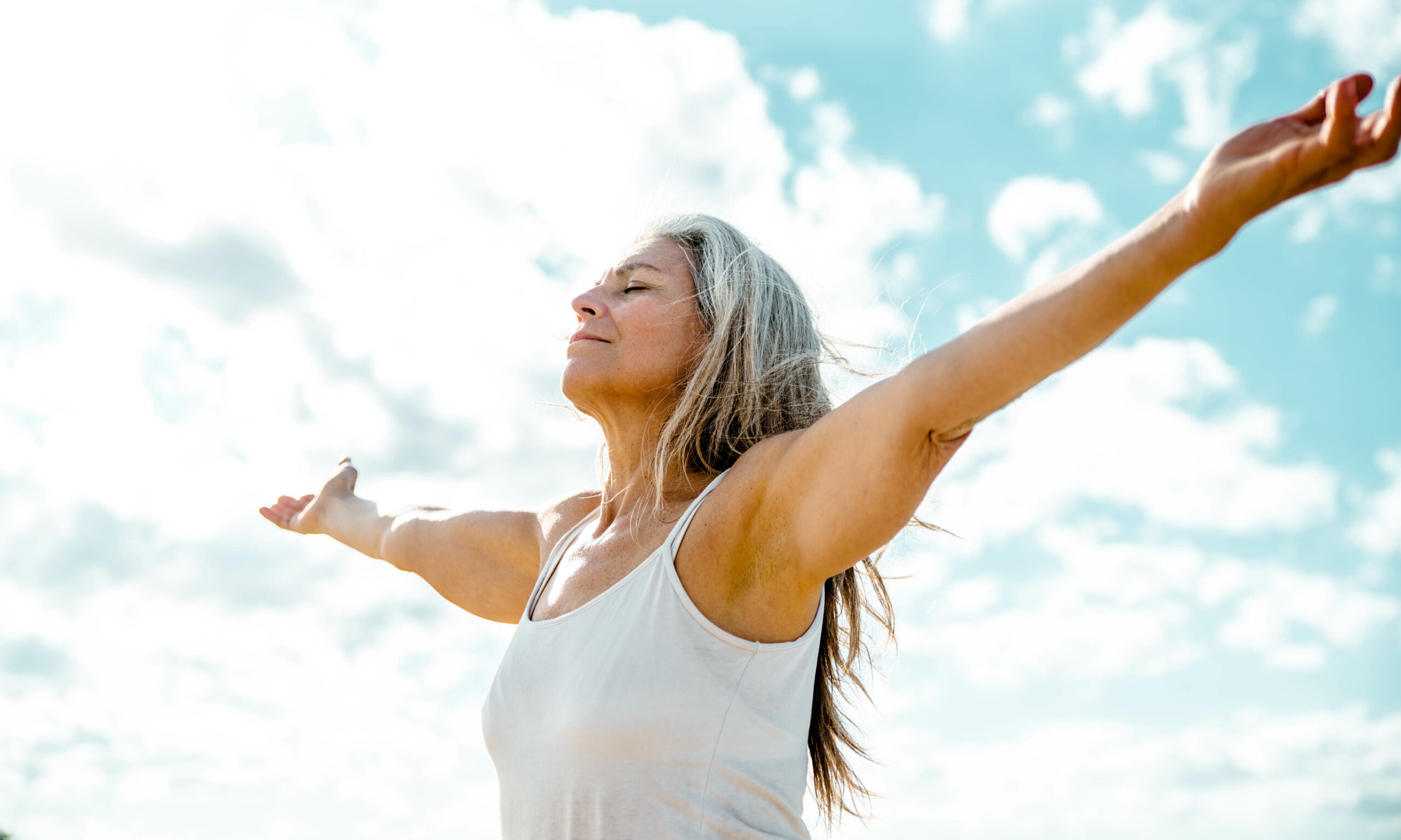 Joyful senior woman enjoying freedom standing with open arms and