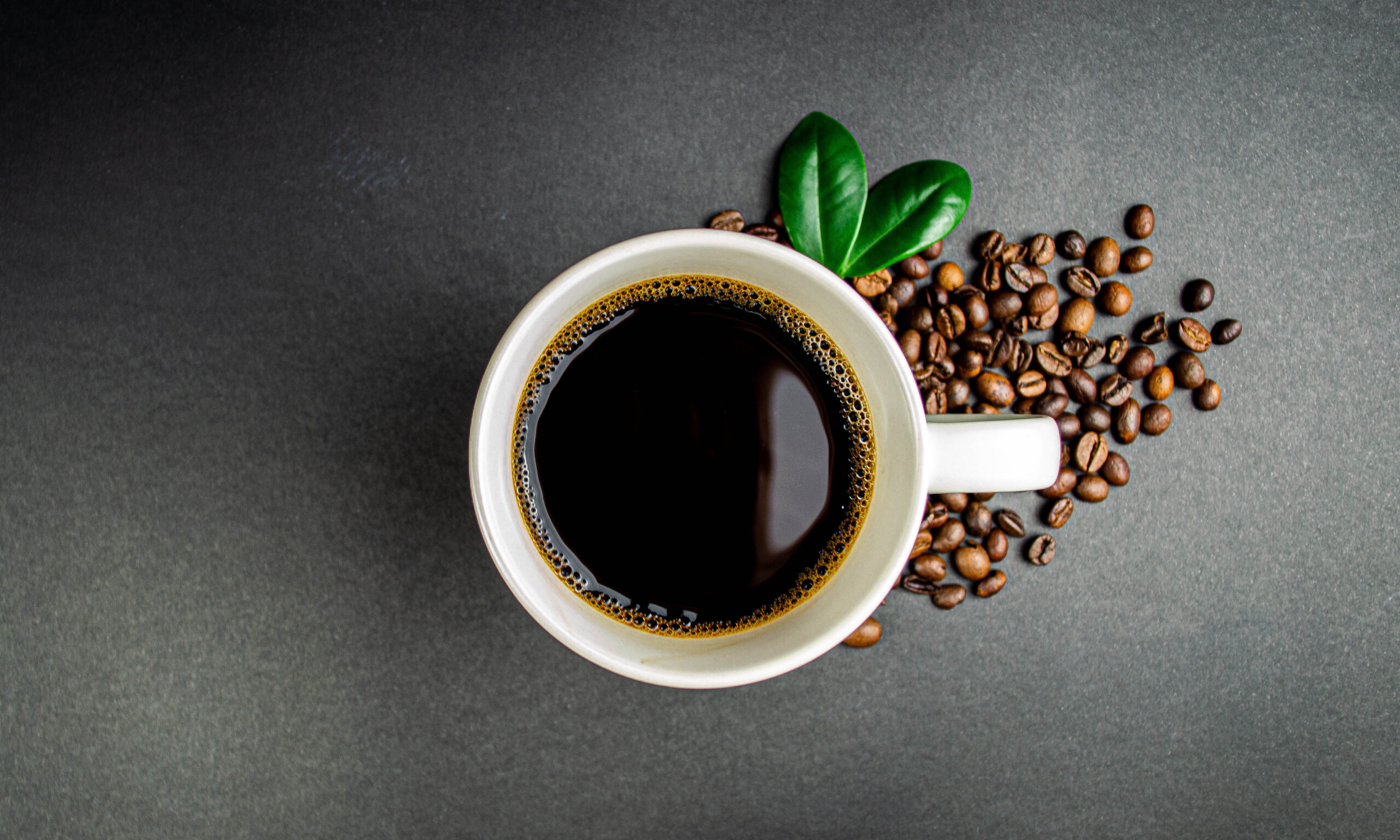 Cup of coffee with roasted beans and green leaves on black backg