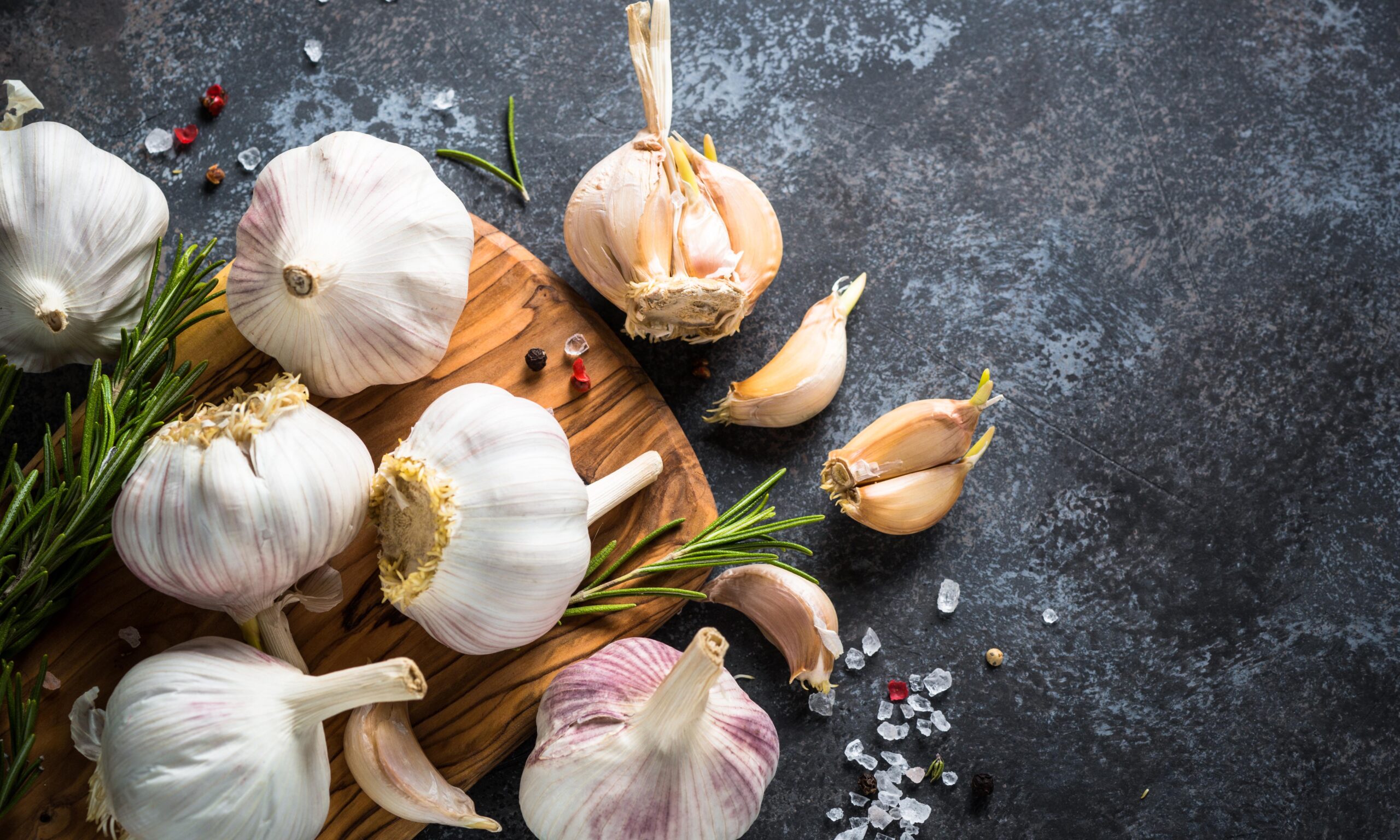 Garlic cloves with spices and herbs on a dark stone background. Top view, Copy space.