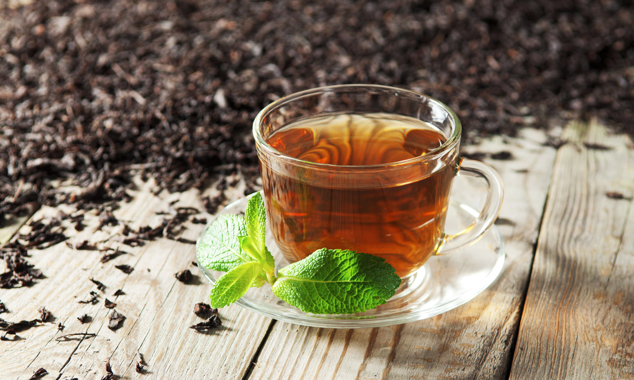 Black tea in a glass cup and saucer on a wooden table. Next to a cup of black tea scattered dry tea