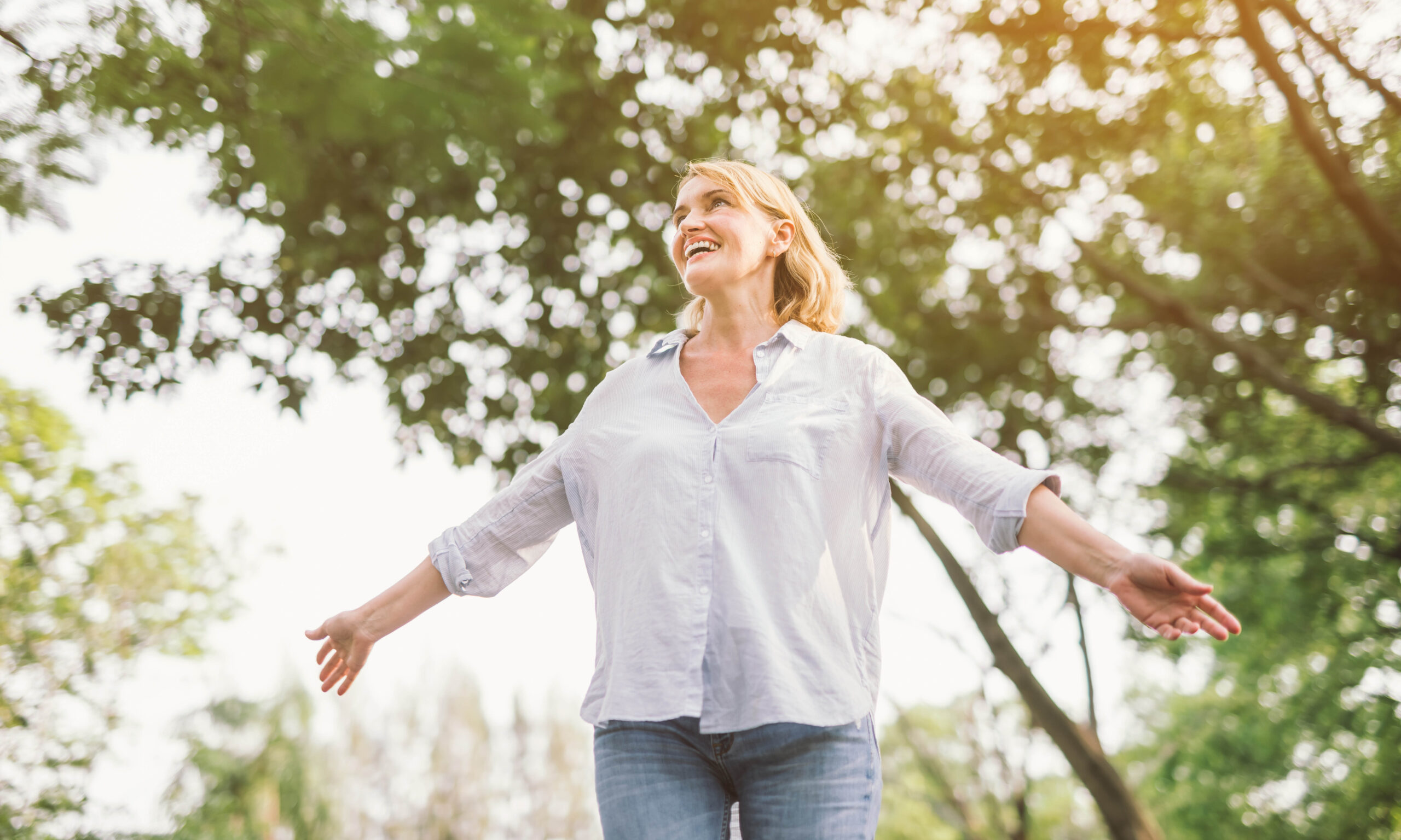happy woman in spring or summer forest park open arms with happiness, hope and vitality. Caucasian girl relaxing and enjoying life on nature outdoors.