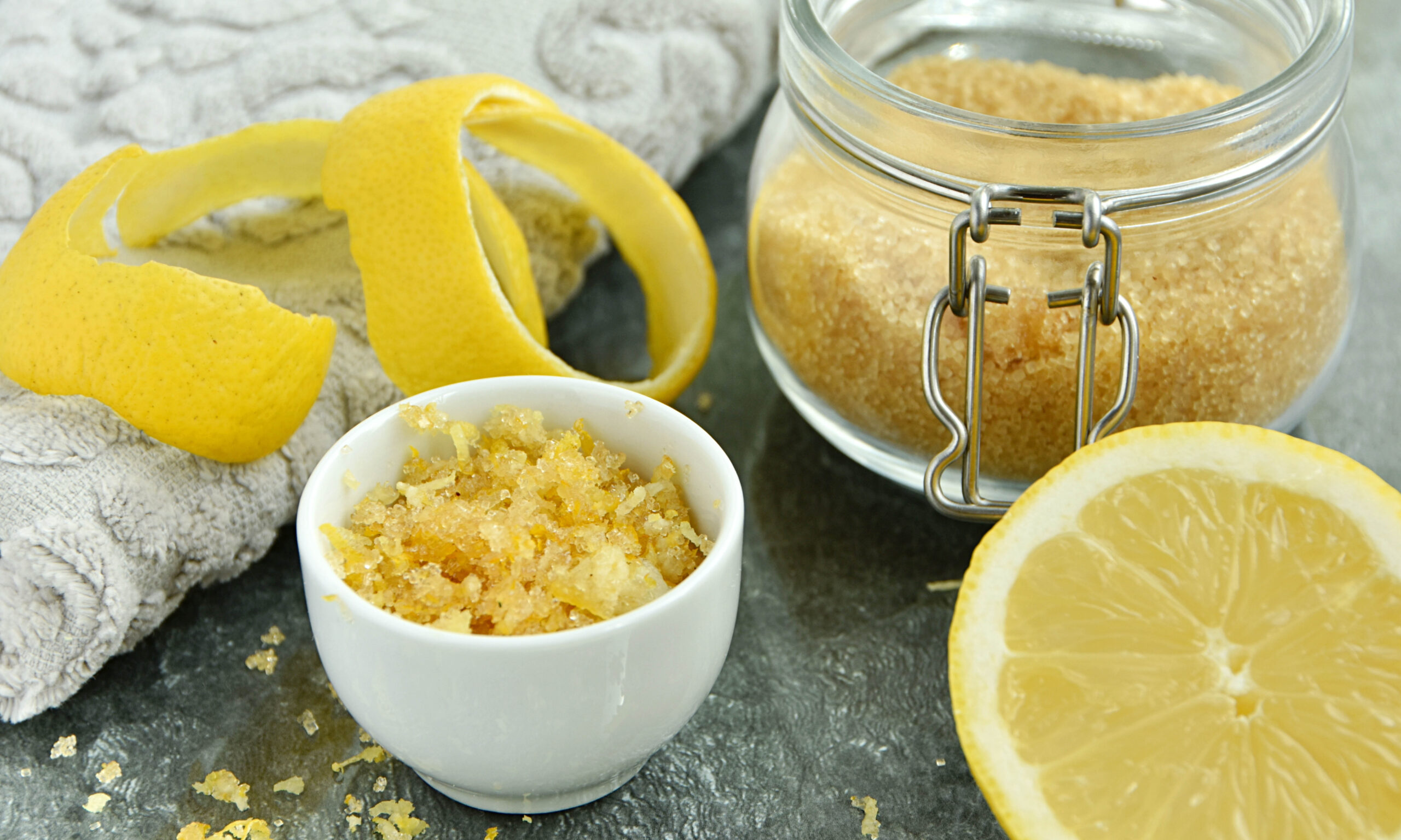 Homemade lemon peel and sugar lip scrub in small bowl and ingred