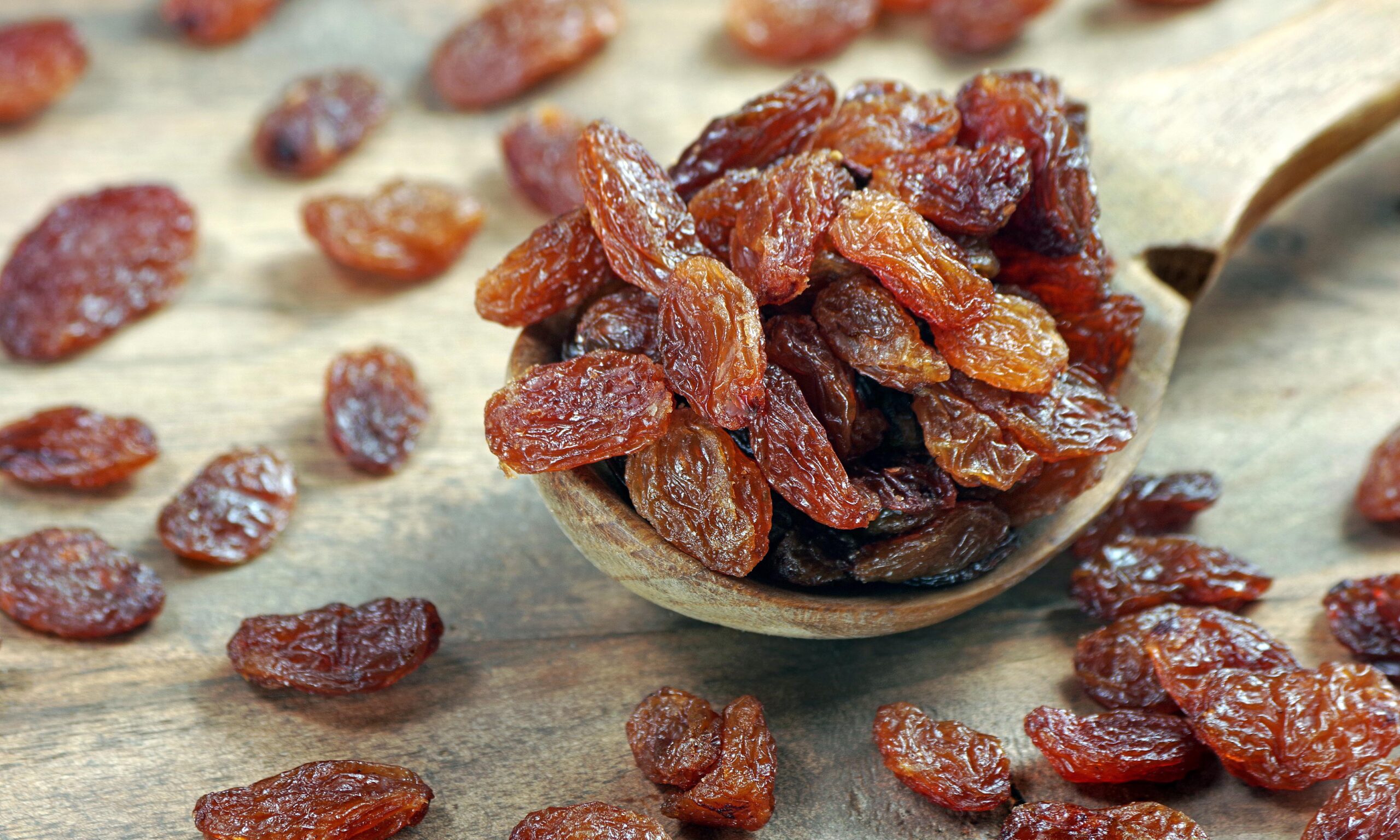 raisins in a spoon on a wooden table. heap of black raisins clos