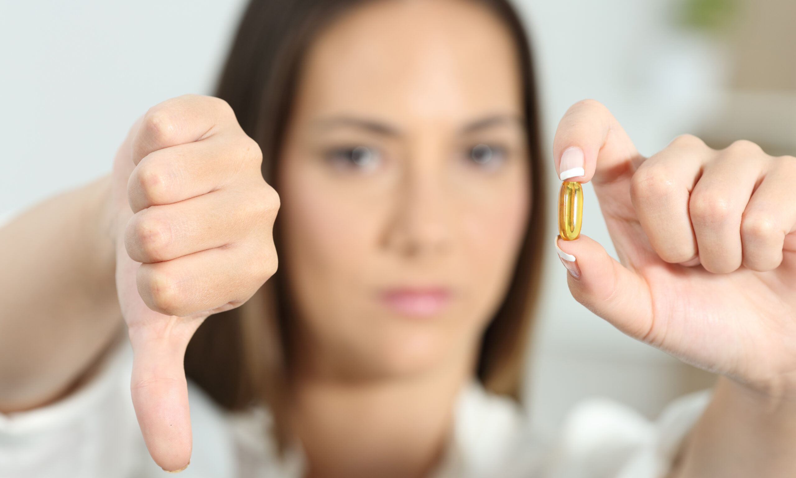 Close up of an angry woman showing a vitamin supplement with thumbs down