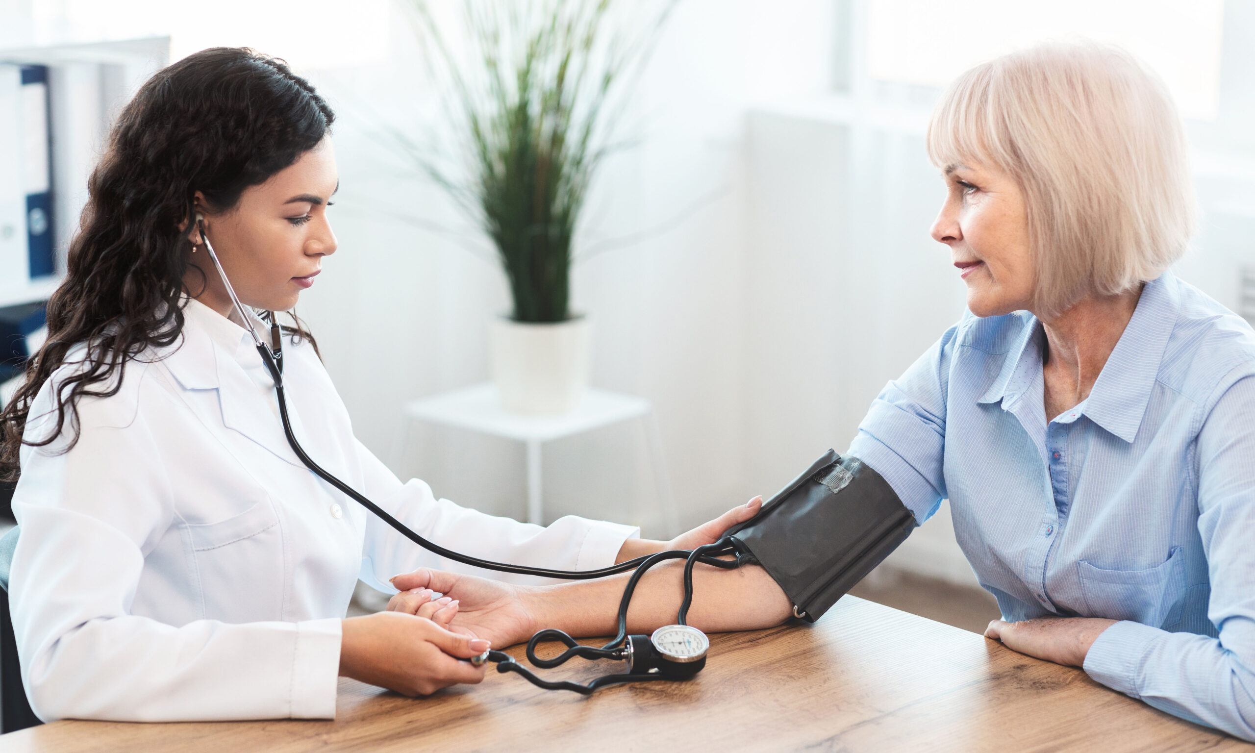 Cardiology. Mexican doctor measuring blood pressure of senior woman, checking patient, free space, panorama