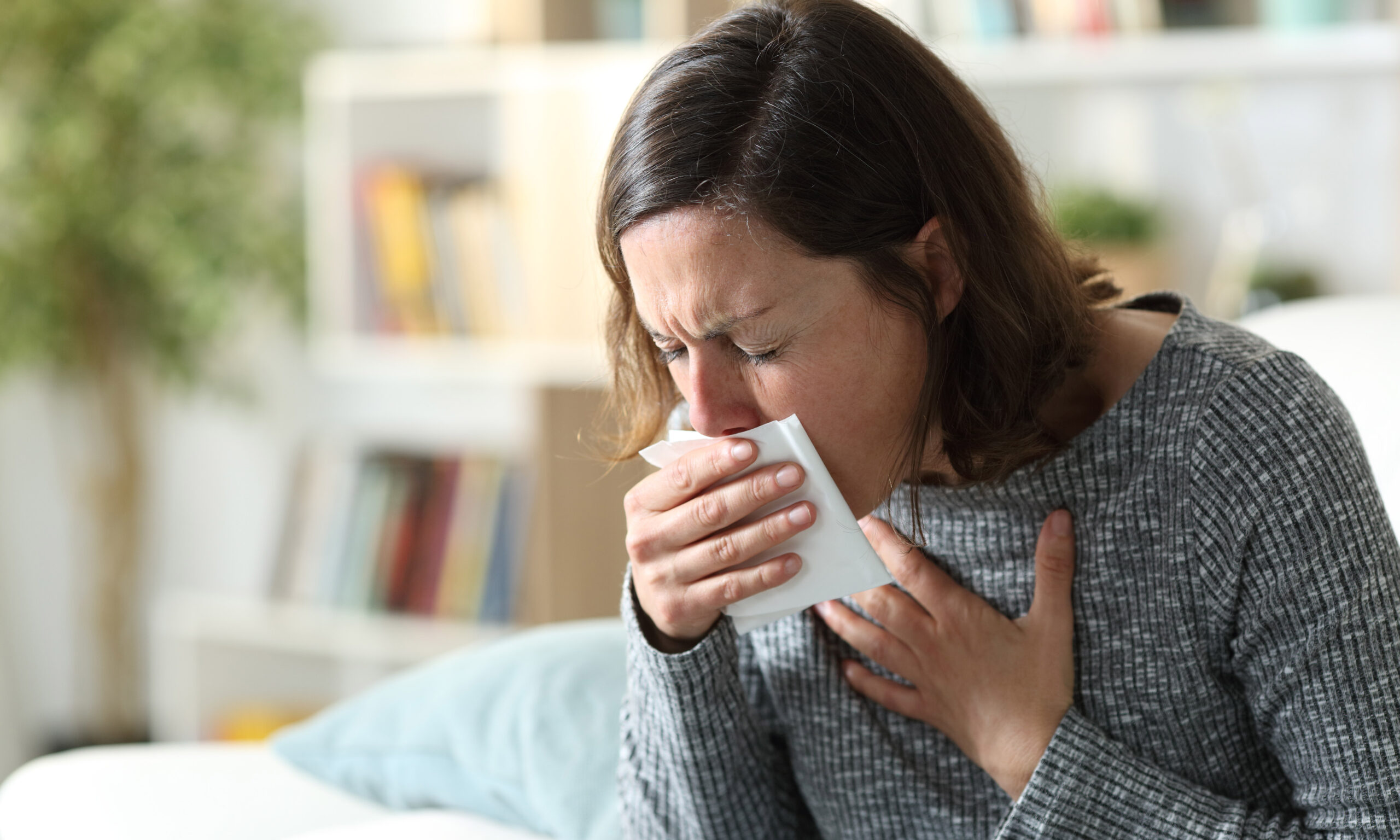 Sick adult woman coughing covering mouth with tissue at home