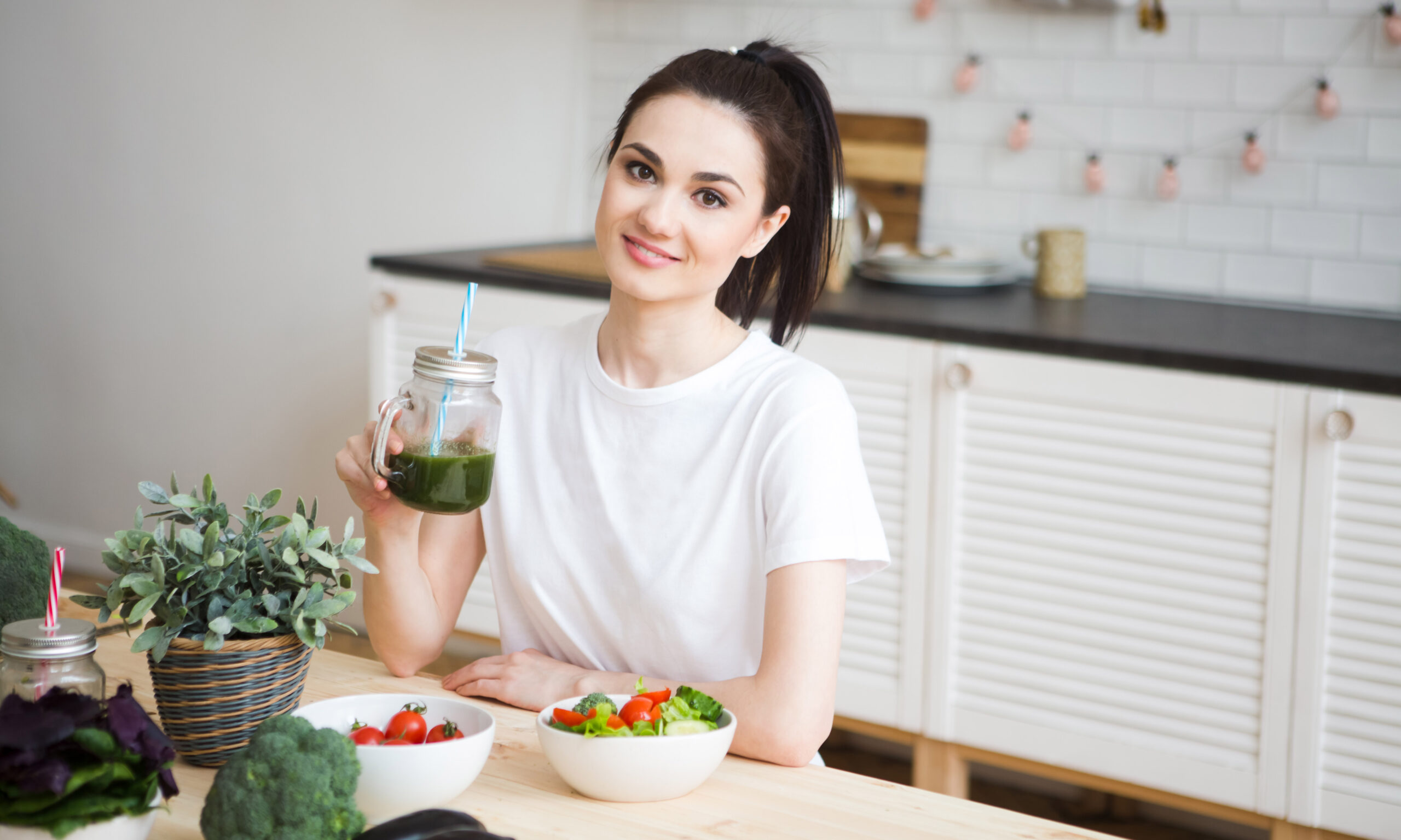 Smiling young woman drinking green smoothie juice in kitchen. He