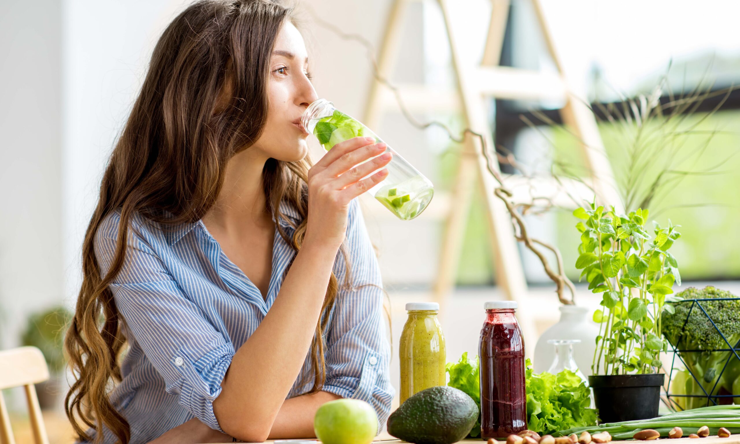 Beautiful woman sitting with drinks and healthy green food at home. Vegan meal and detox concept