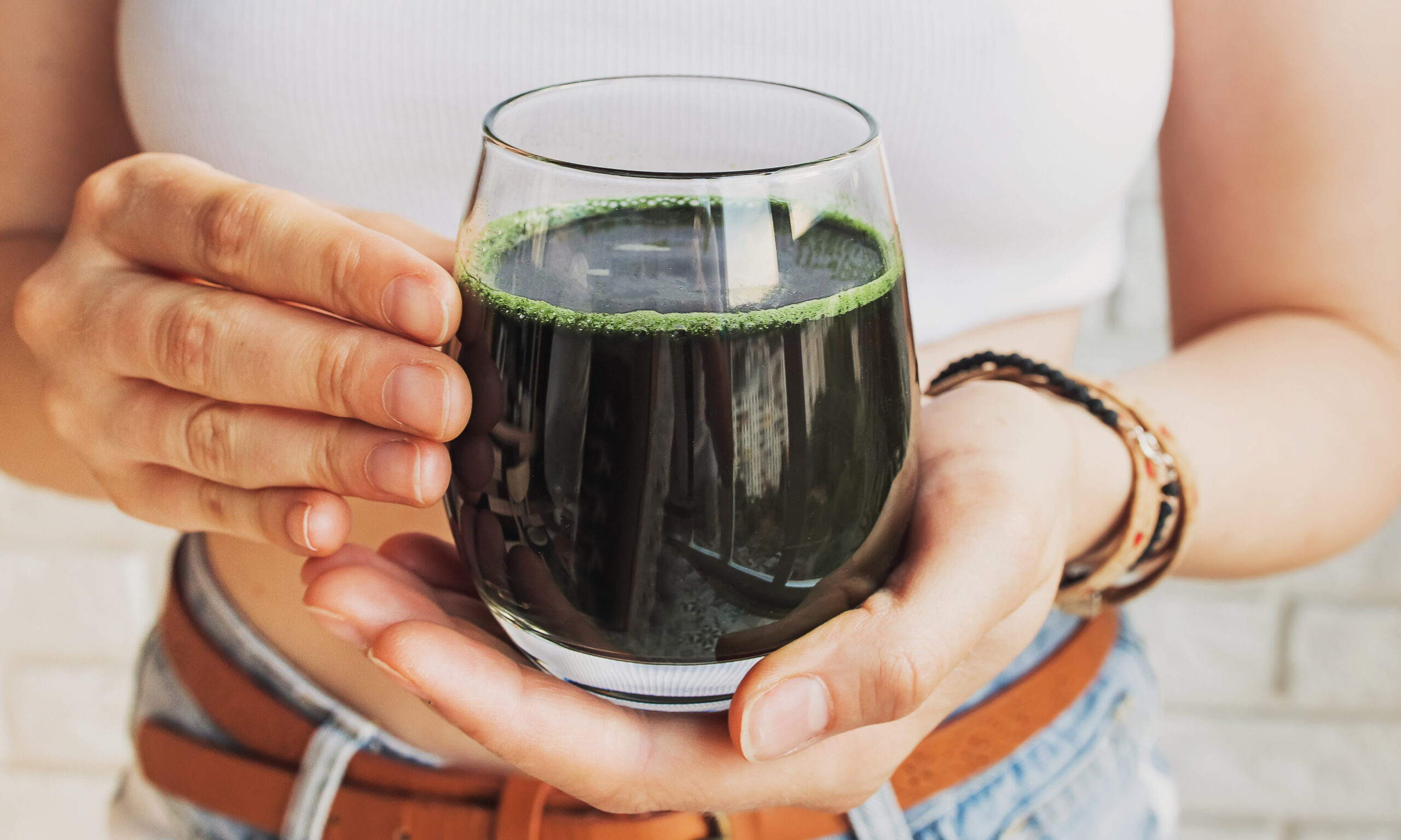 Woman holding glass with healthy spirulina drink or green smoothie close-up