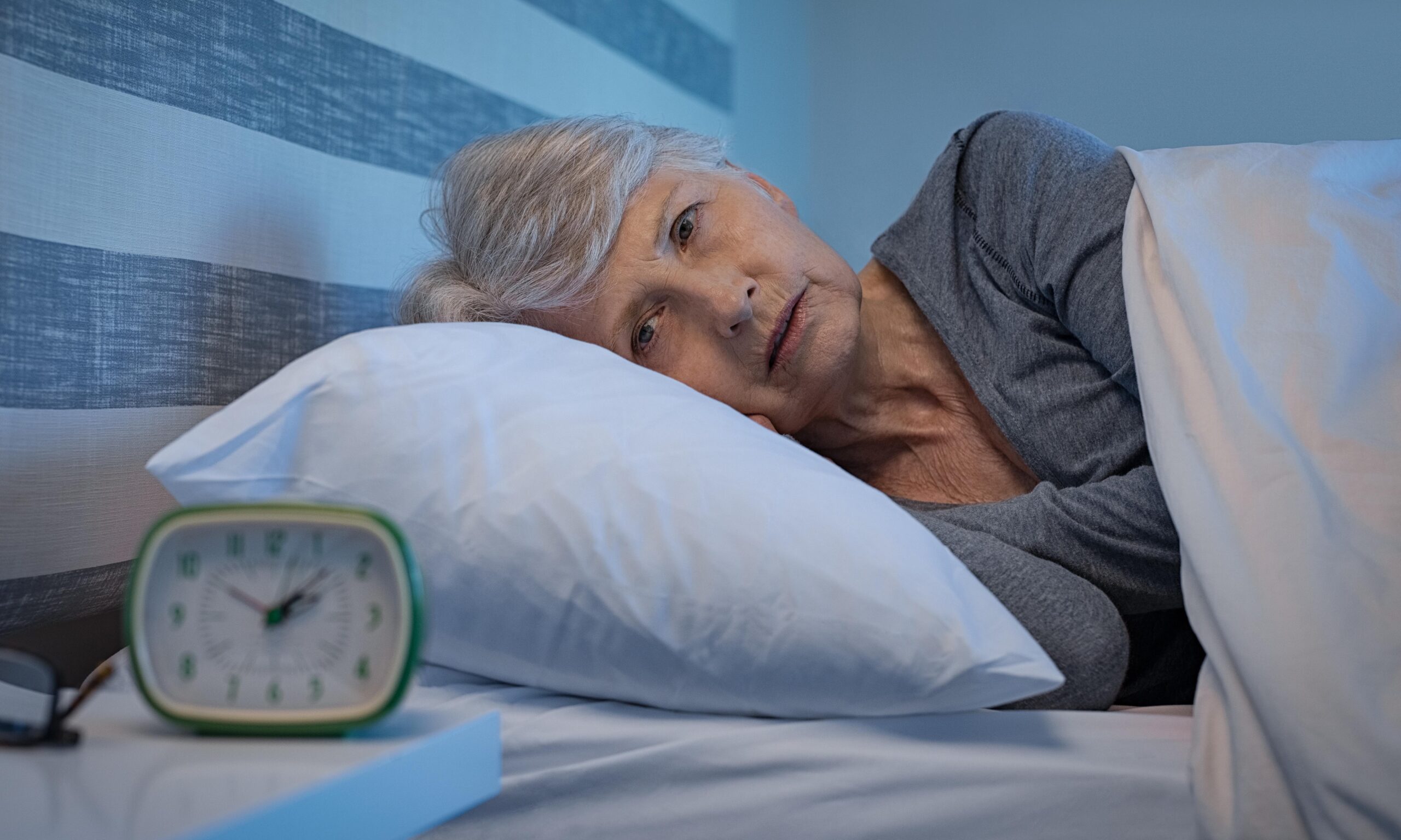 Worried senior woman in bed at night suffering from insomnia. Old woman lying in bed with open eyes. Mature woman unable to sleep at home.