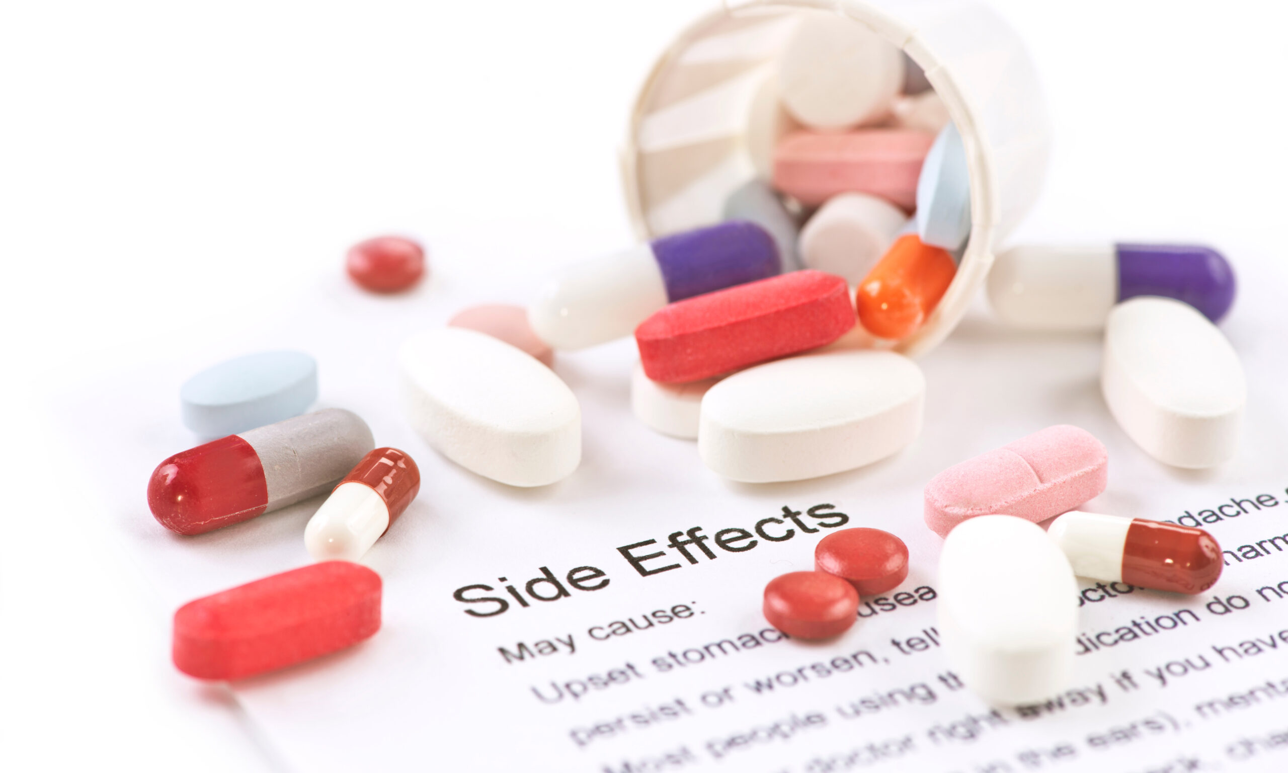 Assorted pills and capsules with side effects information sheet.