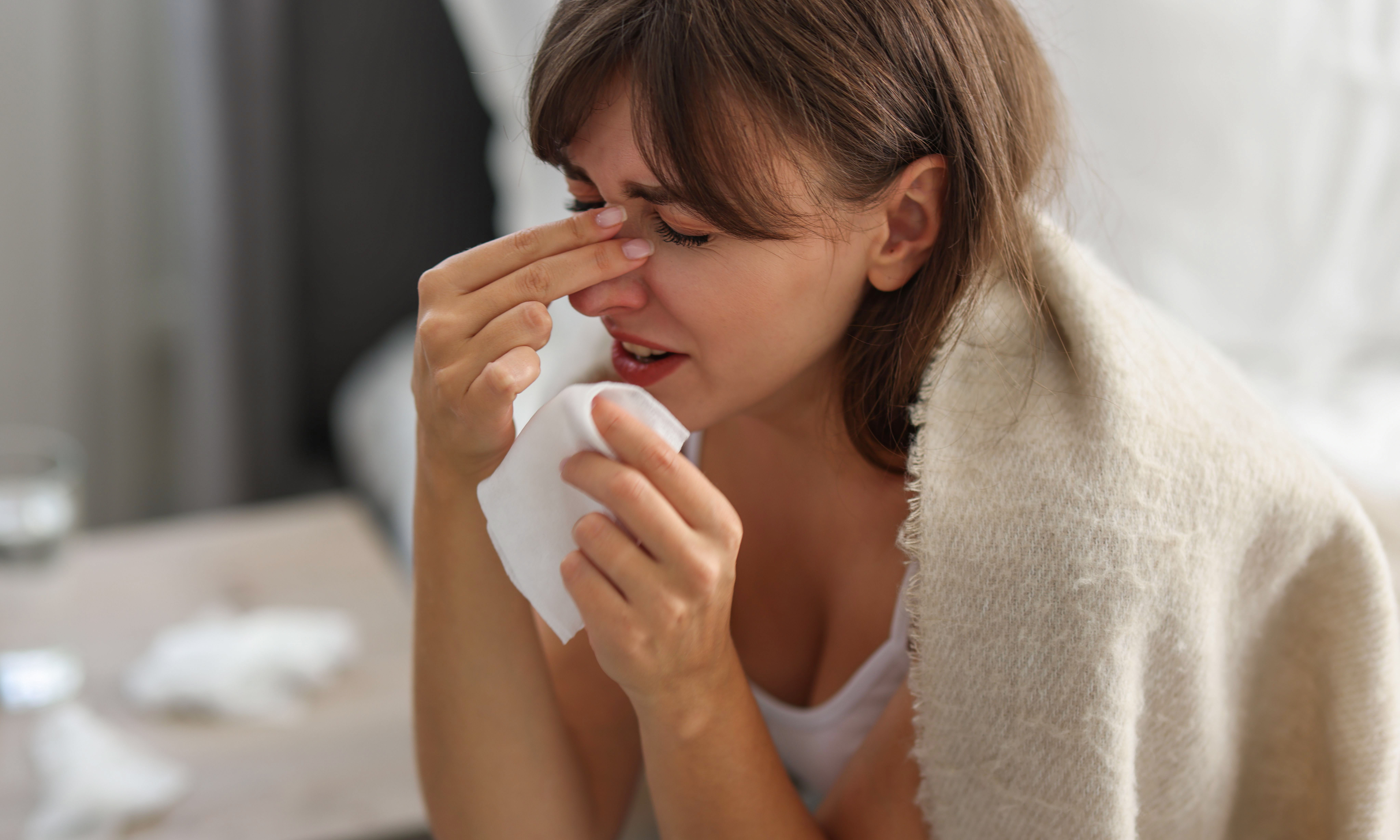 Woman wrapped in blanket suffering from sinusitis at home
