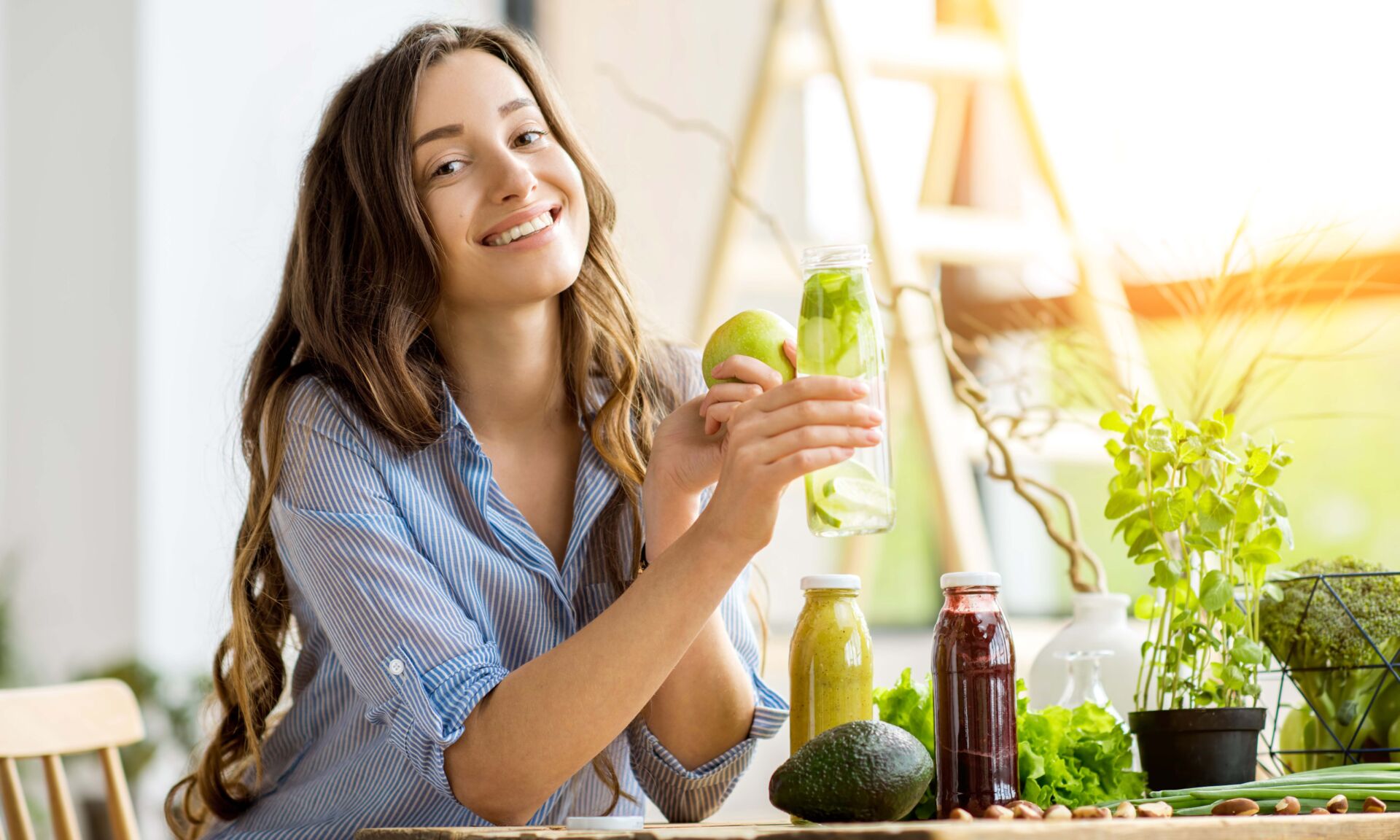 Beautiful happy woman sitting with drinks and healthy green food at home. Vegan meal and detox concept