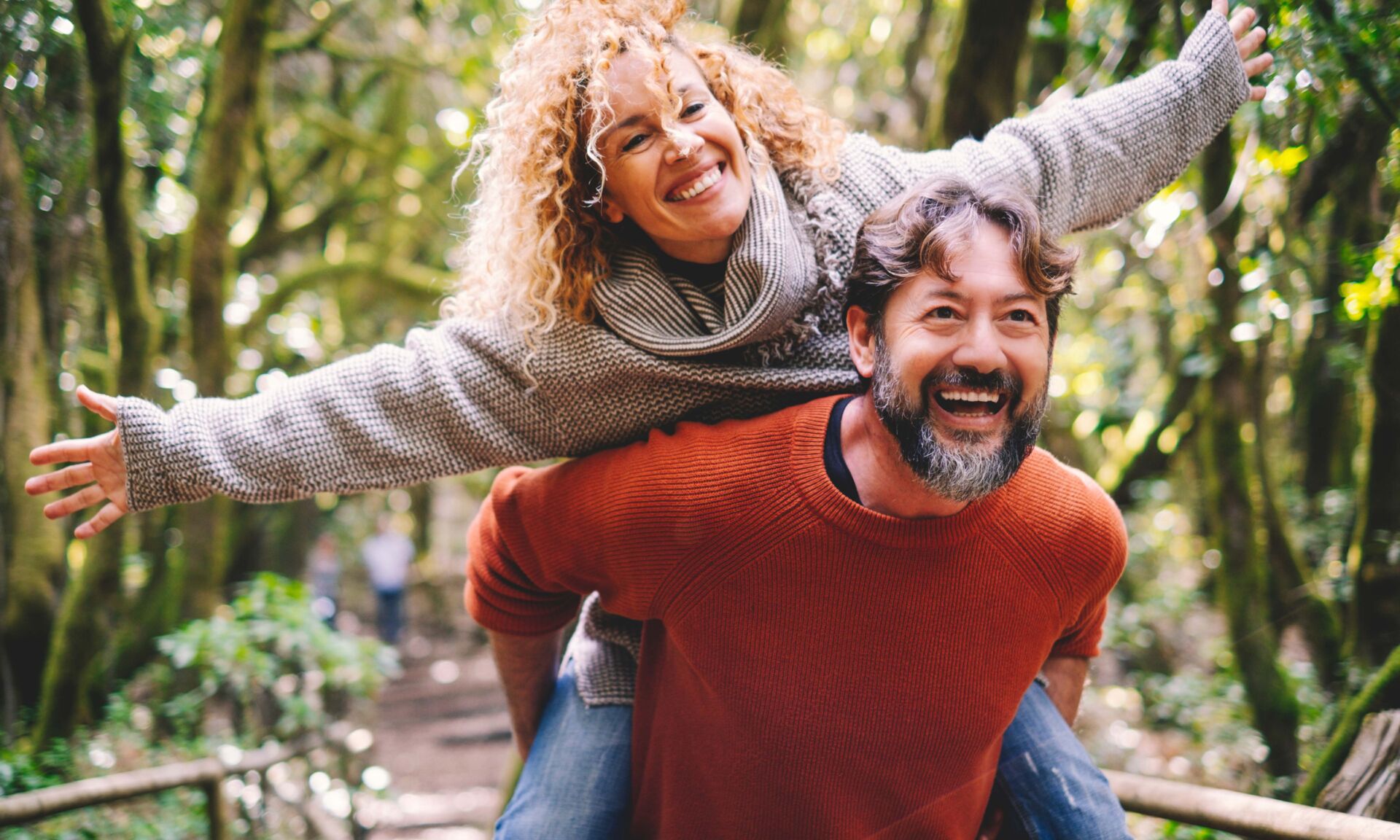 Overjoyed adult couple have fun together at outdoor park in leisure activity. Man carrying woman in piggyback and laugh a lot. Love and life mature people lifestyle concept. Enjoying vacation nature