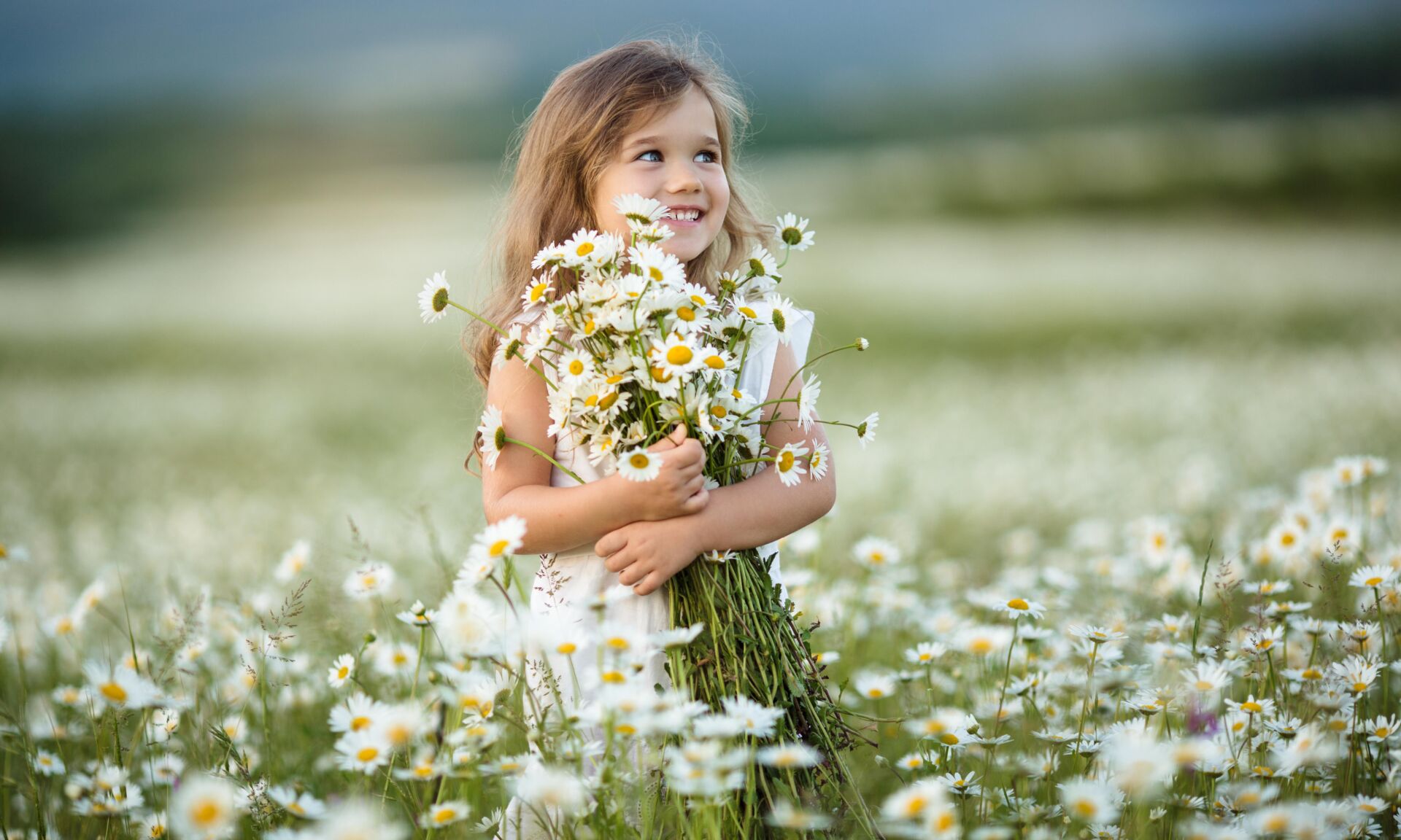 Little happy girl having fun in a field of camomile flowers