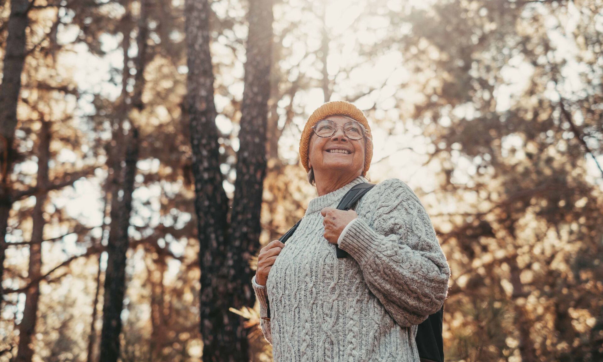 Head shot portrait close up of middle age caucasian woman walking and enjoying nature in the middle of trees in forest. Old mature female wearing glasses trekking and discovering.