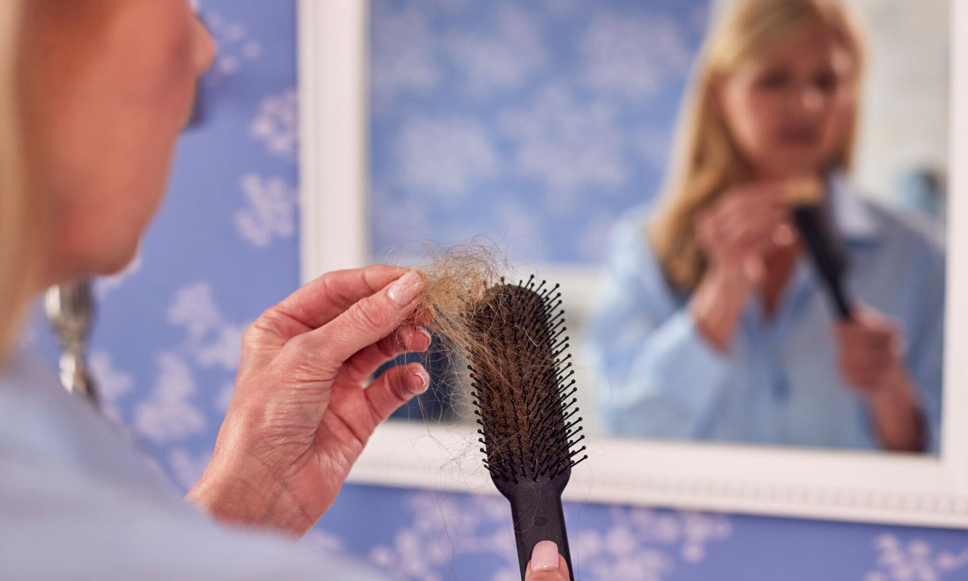 Menopausal Mature Woman Suffering Hair Loss Brushing Hair In Mirror At Home