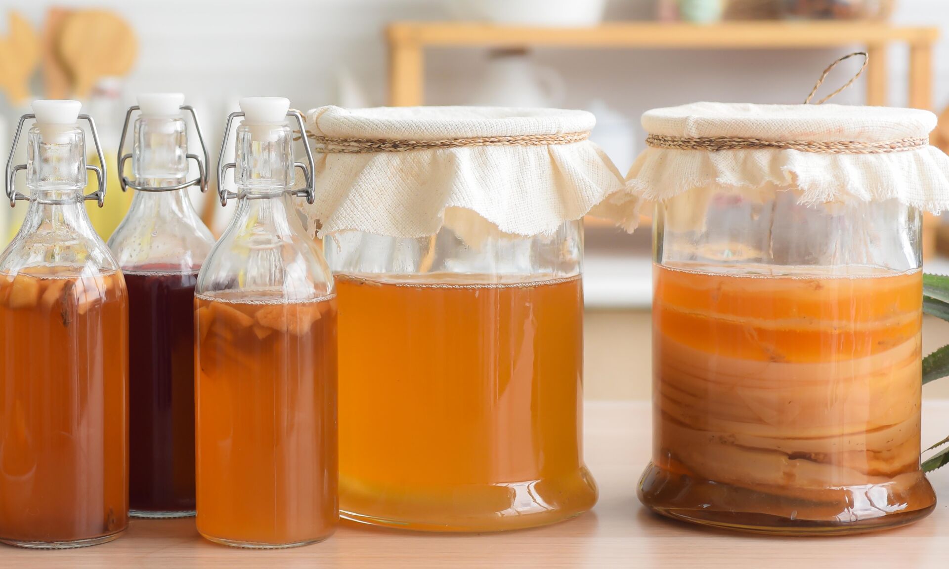 Homemade fermented raw kombucha tea, variety of flavors in bottles and glass jars mix with a fruit juice and scoby on wooden table in kitchen. Healthy natural probiotic drink.