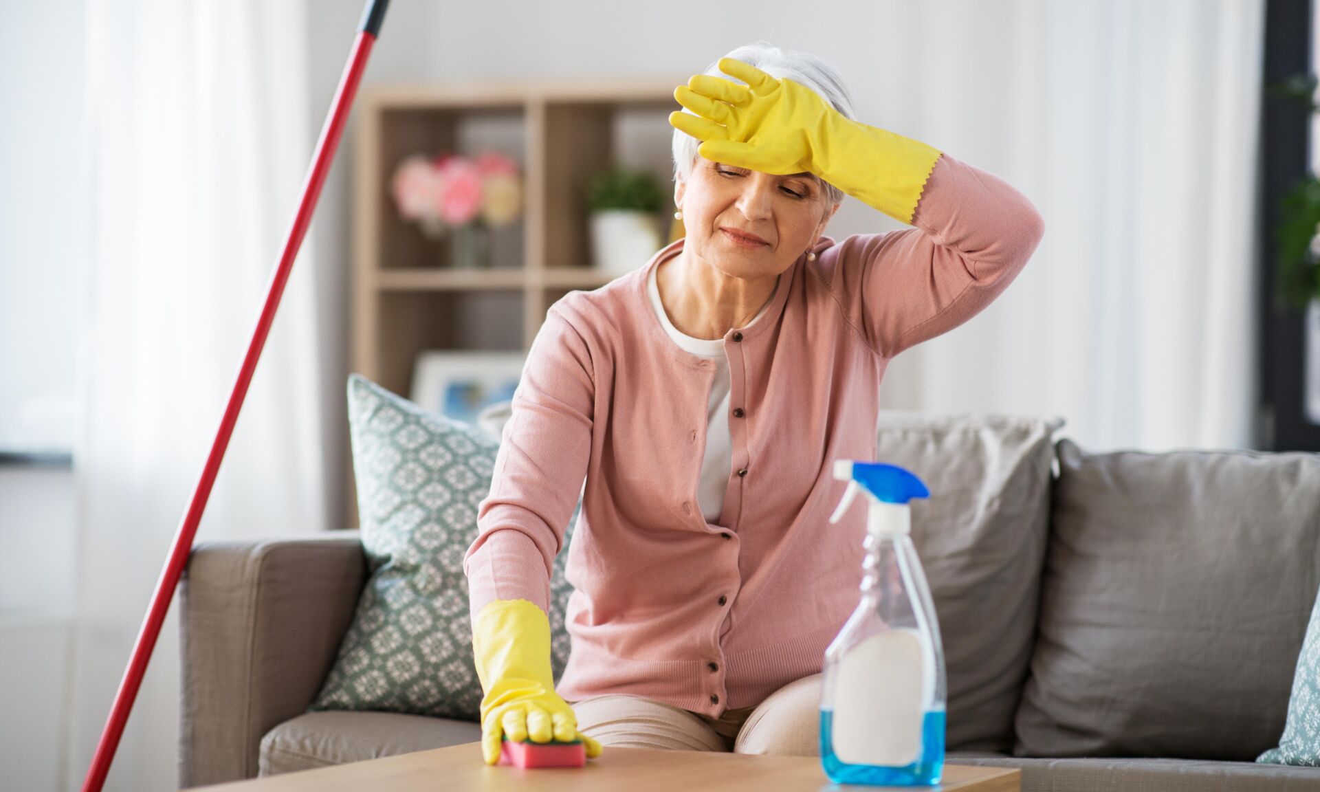 household and people concept - tired senior woman with detergent and sponge cleaning table at home