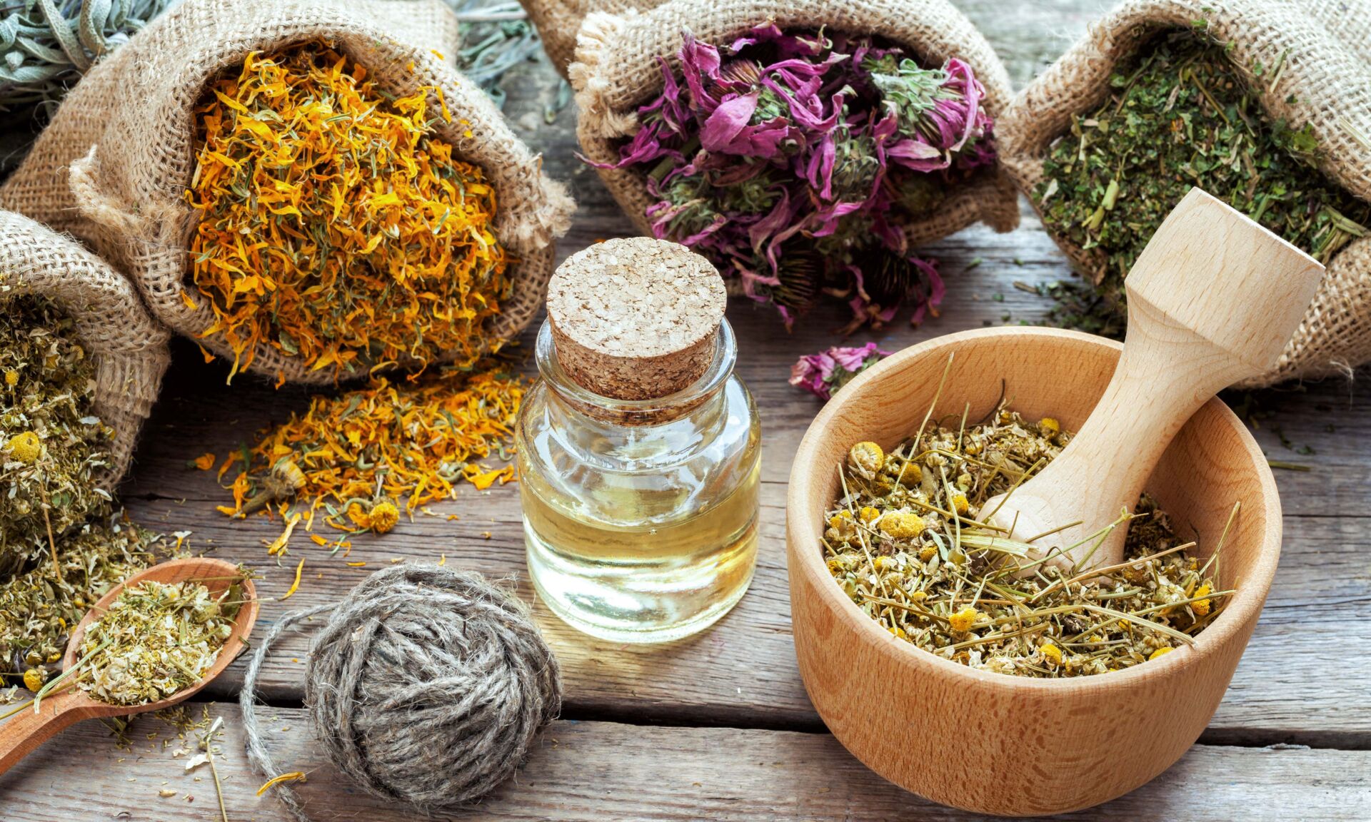 Healing herbs in hessian bags, mortar with chamomile and essential oil on wooden table, herbal medicine.