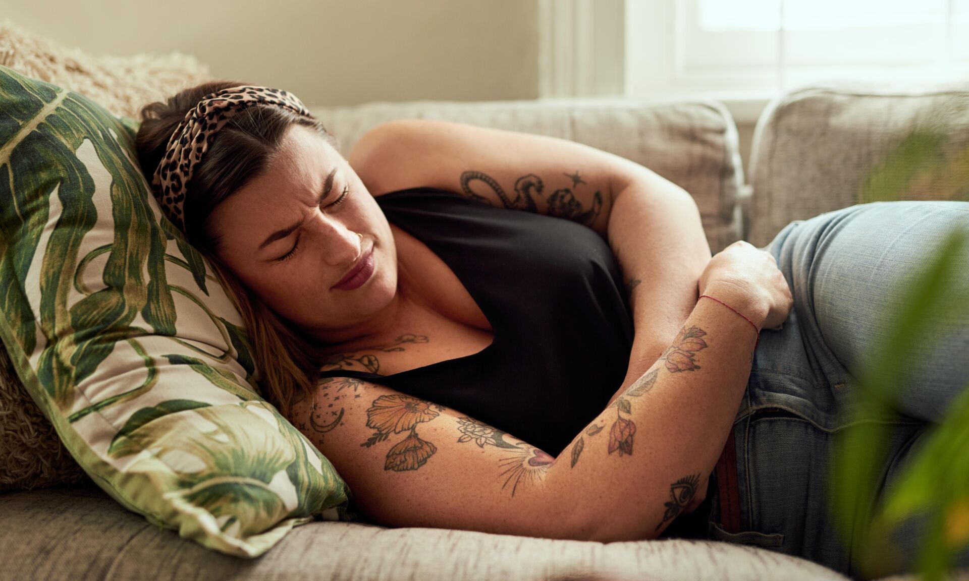 Sick, woman and stomach pain on sofa in home with uncomfortable ache, pms bloating and period cramps. Person, menstruation and indigestion with ibs discomfort, endometriosis and nausea in apartment.
