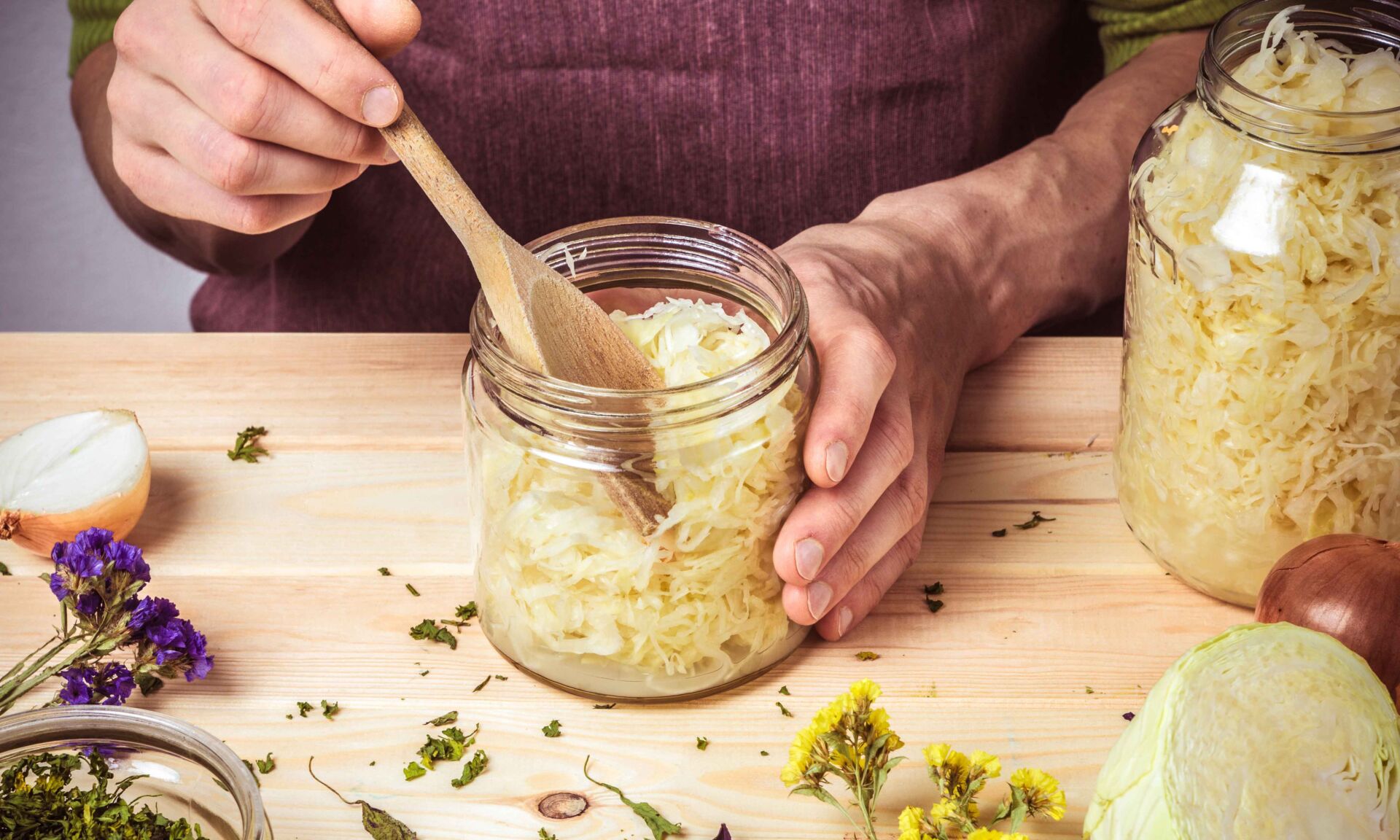 The cook puts sauerkraut in glass jars. On the table are spices,