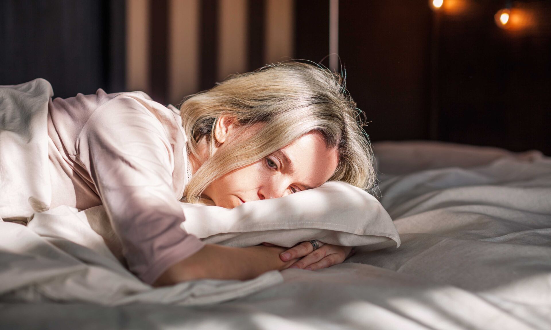 Tired middle aged woman lying in bed can't sleep late at morning with insomnia. Adult lady sick or sad depressed sleeping at home.