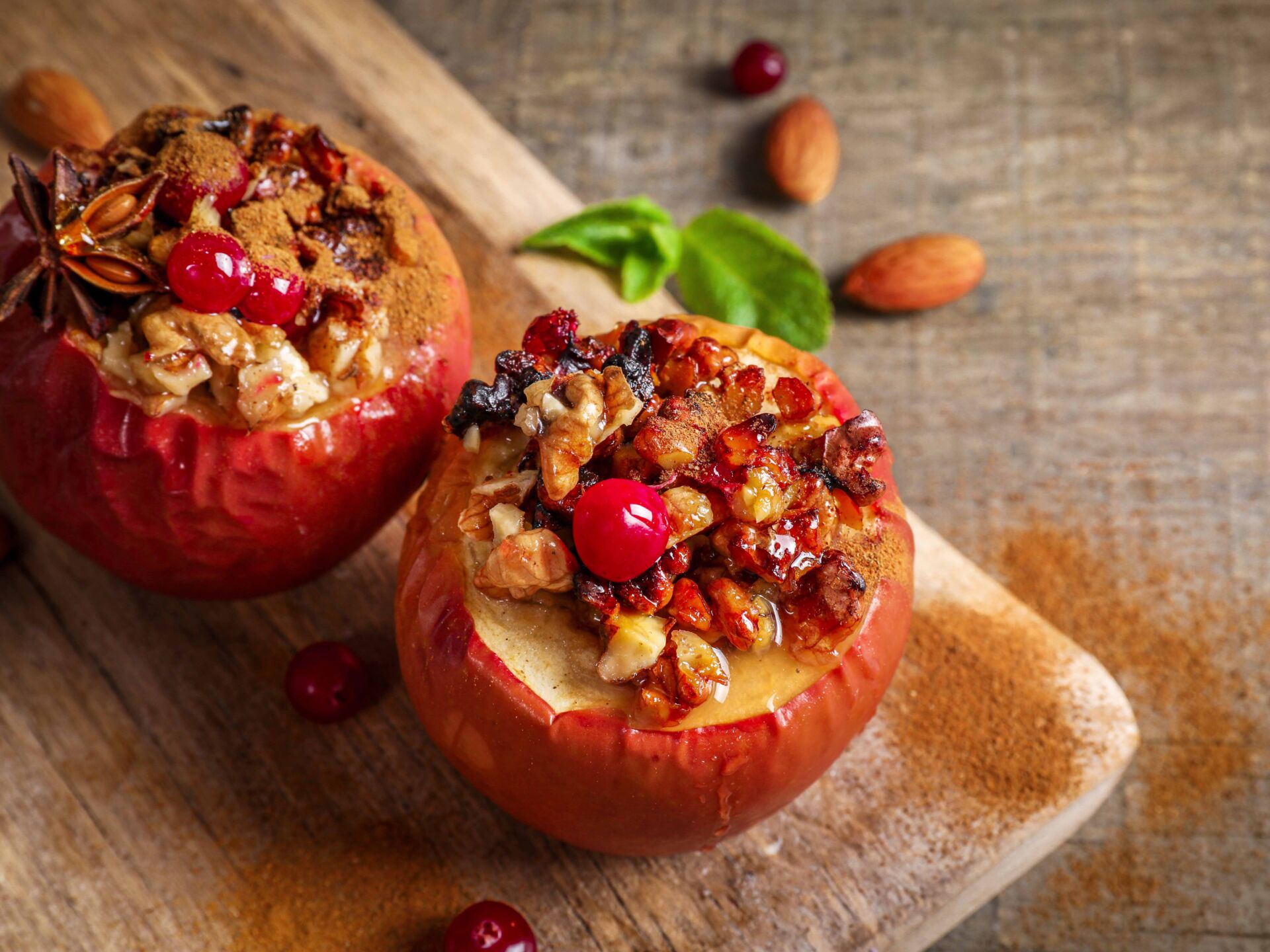 Baked apples stuffed with walnuts and honey on wooden cutting board on wooden background.