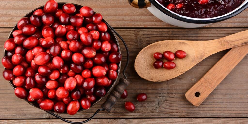 Overhead of a bucket of cranberries and a pot full of whole cranberry sauce on a rustic wooden table. Cranberry sauce is a traditional Thanksgiving side dish. Horizontal format.